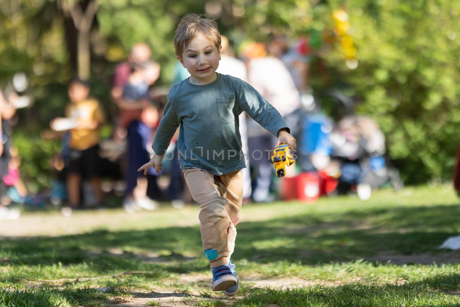 A young boy is running through a park with a toy bus in his hand by Studia72