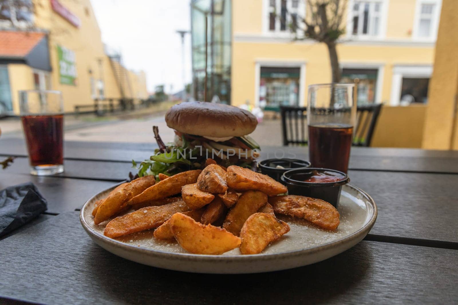Plate with burger and french fries, ketchup and mayonnaise and cola on the table in the restaurant.