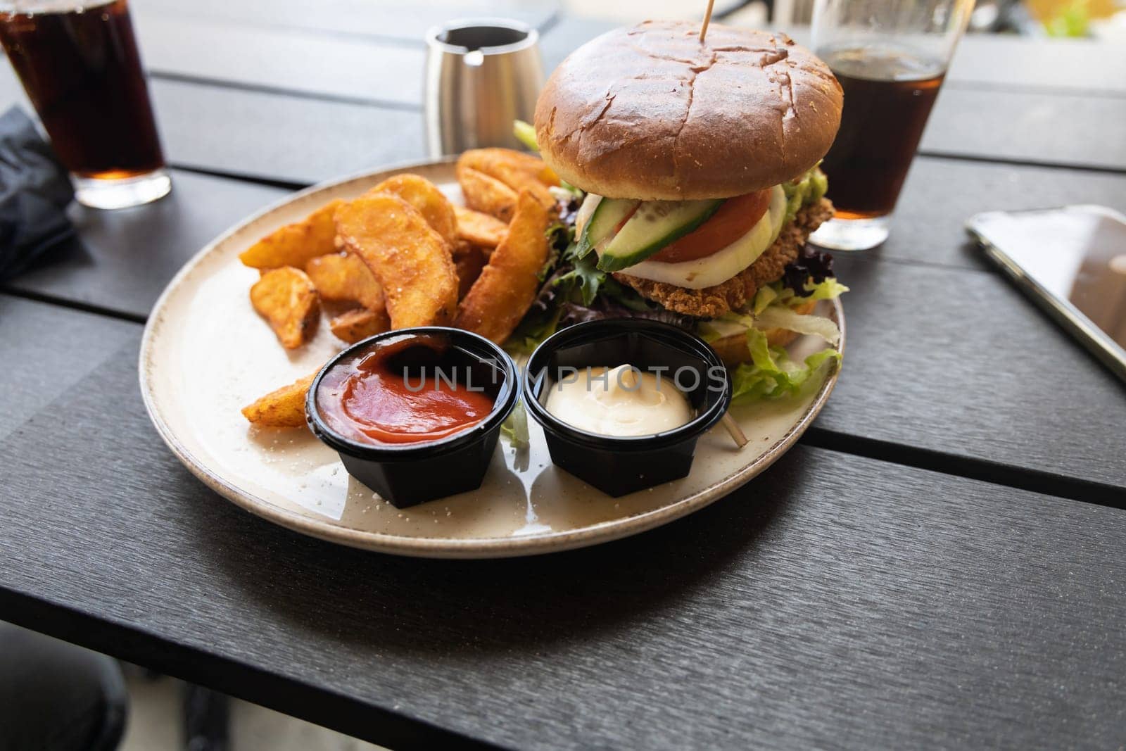 Plate with burger and french fries, ketchup and mayonnaise and cola on the table in the restaurant.