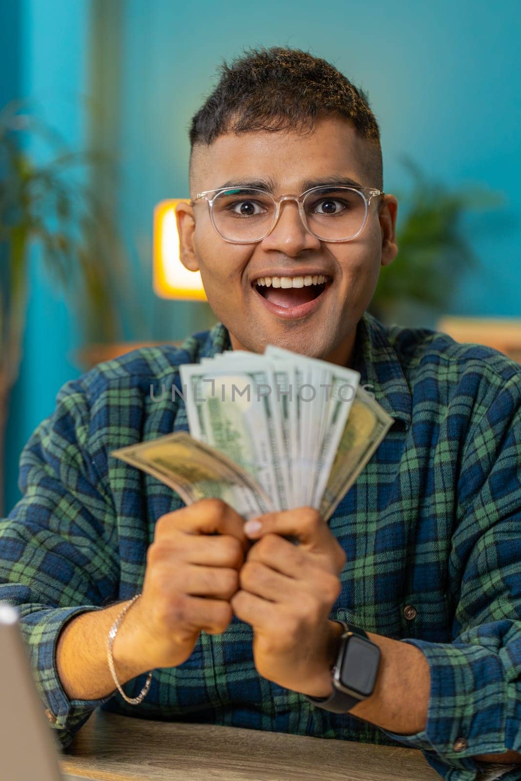 Rich pleased happy Indian man waving money dollar cash banknotes bills like a fan success business career lottery winner big income wealth. Amazed guy at home office table workplace. Vertical video