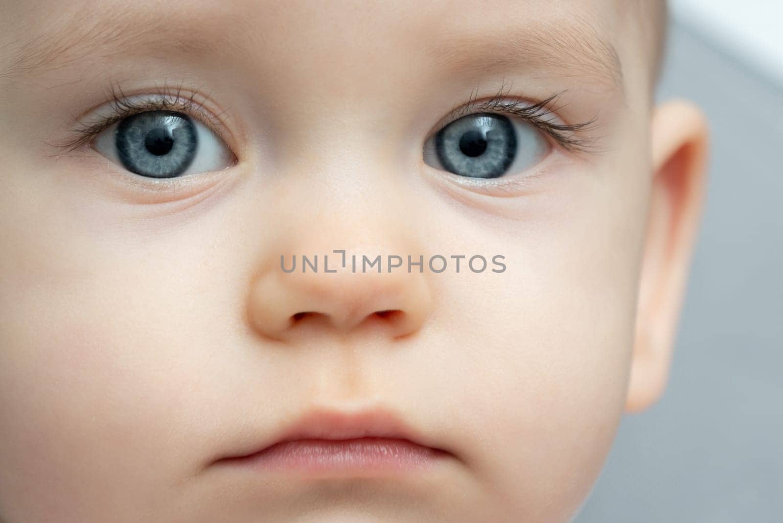 Close-up of a toddler baby gazing at the camera with calm face by Mariakray