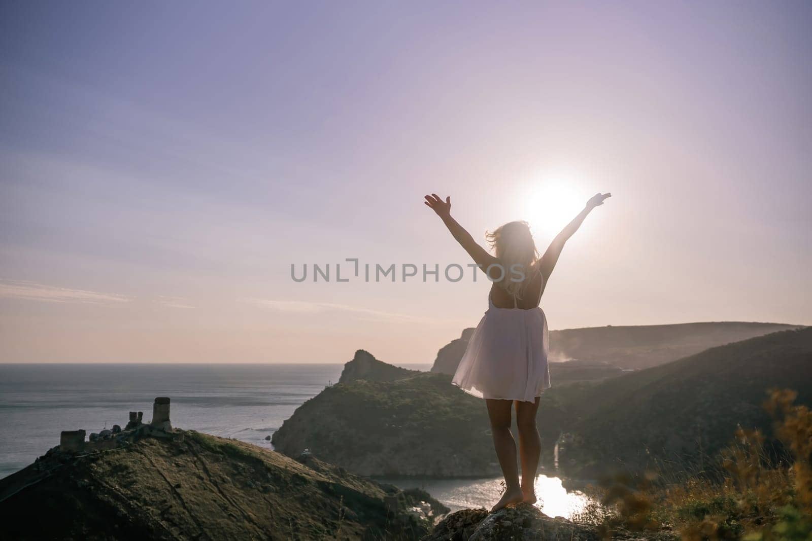 A woman is standing on a hill overlooking a body of water. She is wearing a white dress and she is happy