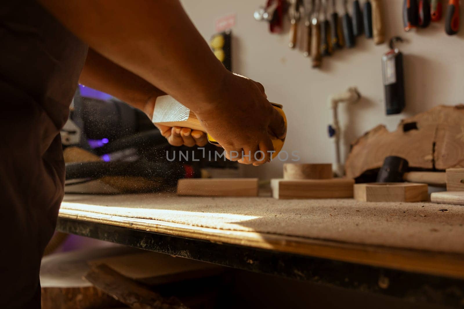 Woodworker at workbench using manual sandpaper to sander timber block, assembling furniture in joinery. Carpenter smoothing piece of wood, spreading sawdust everywhere, close up shot