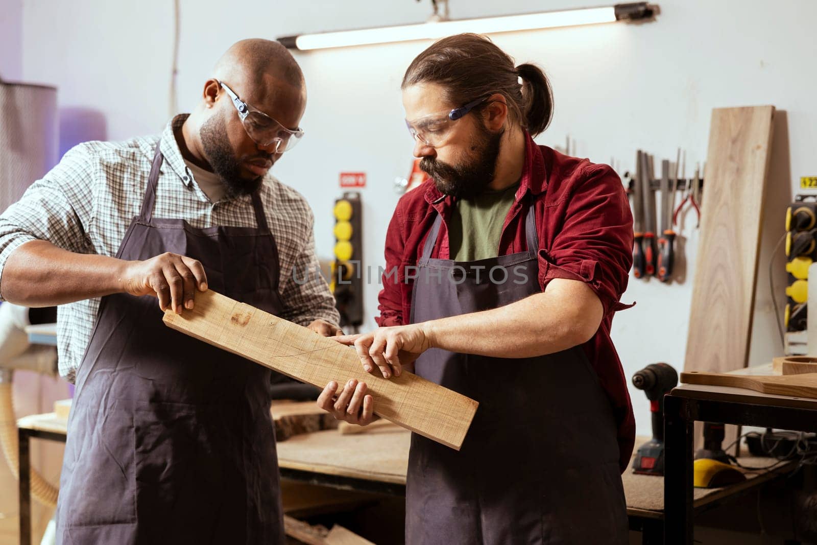 Manufacturer and apprentice wearing safety glasses selecting high quality wood materials. Cabinetmaker and colleague using protective equipment doing quality assurance on lumber piece
