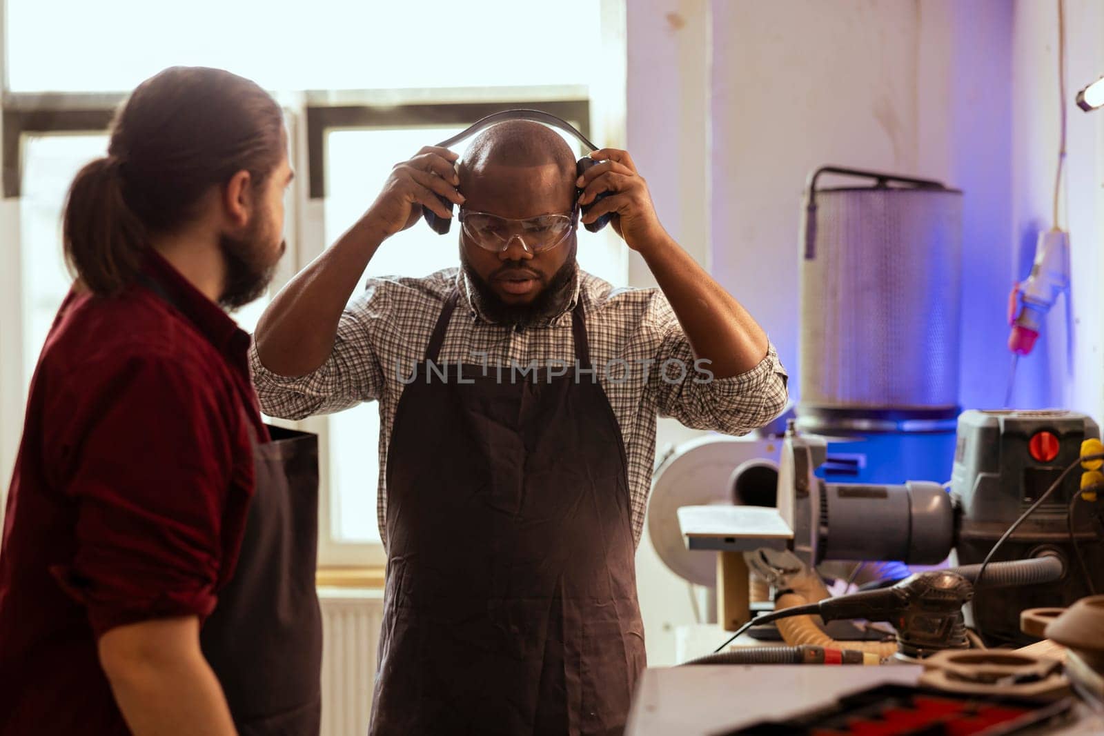 Cabinetmaker making sure apprentice uses safety earmuffs and glasses by DCStudio