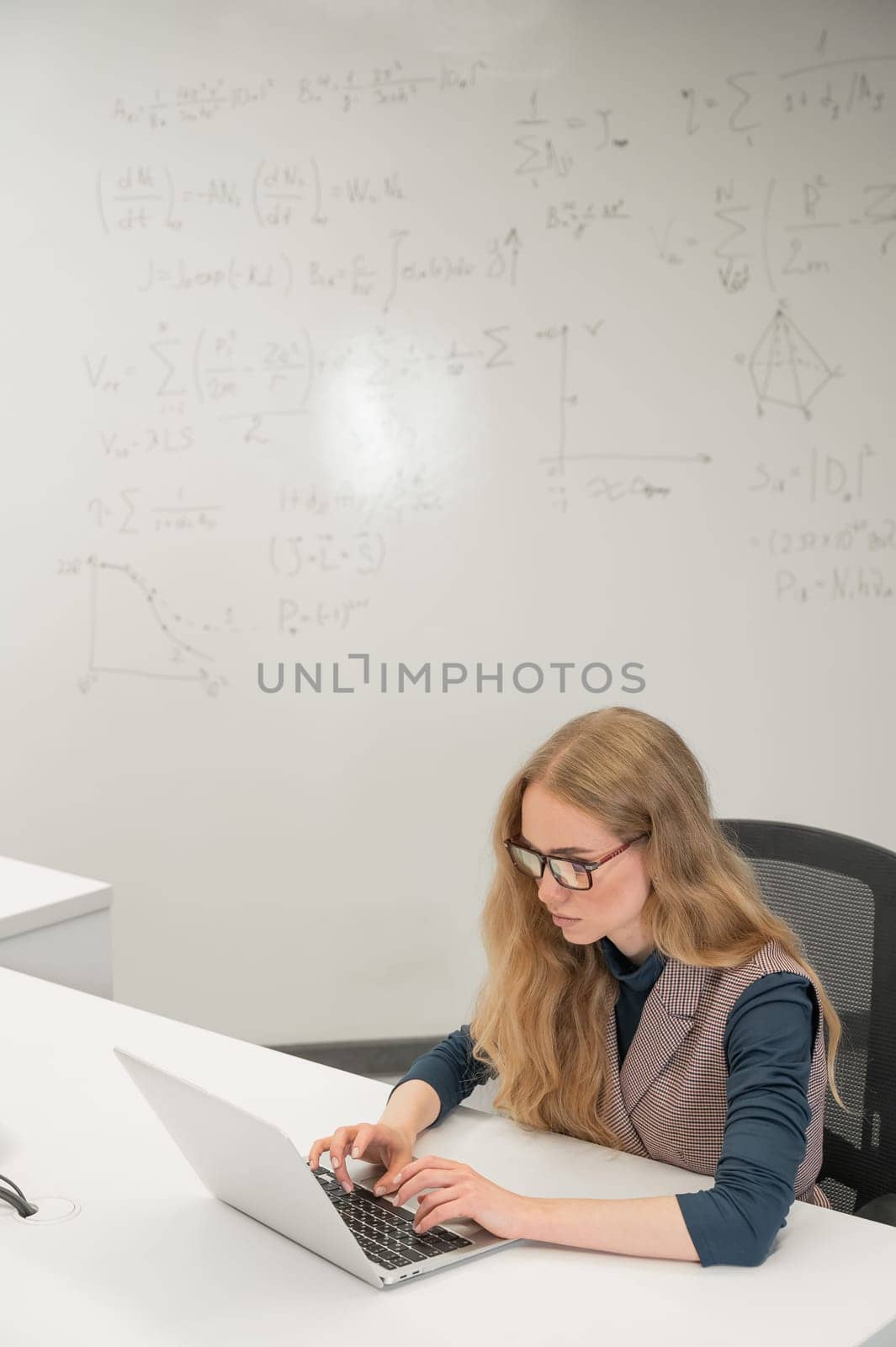 Caucasian woman scientist typing on laptop. White board with formulas. Vertical photo
