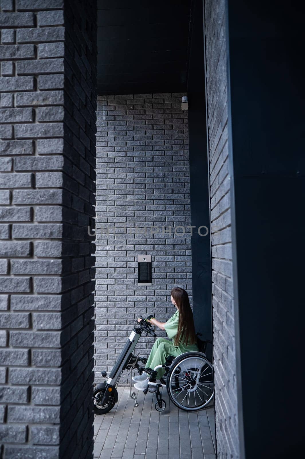 A woman in a wheelchair with an assistive device for manual control enters the entrance. Electric hand bike. by mrwed54