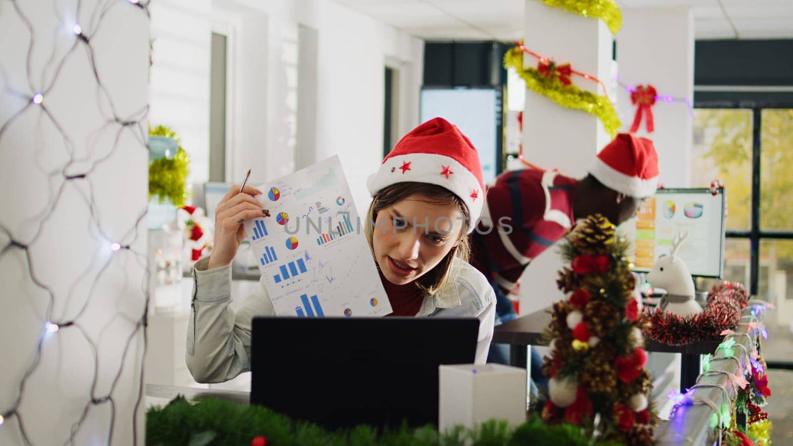 Employee in Christmas decorated office happy to show management positive company profit during videocall. Worker in teleconference meeting talking with managers during xmas holiday season