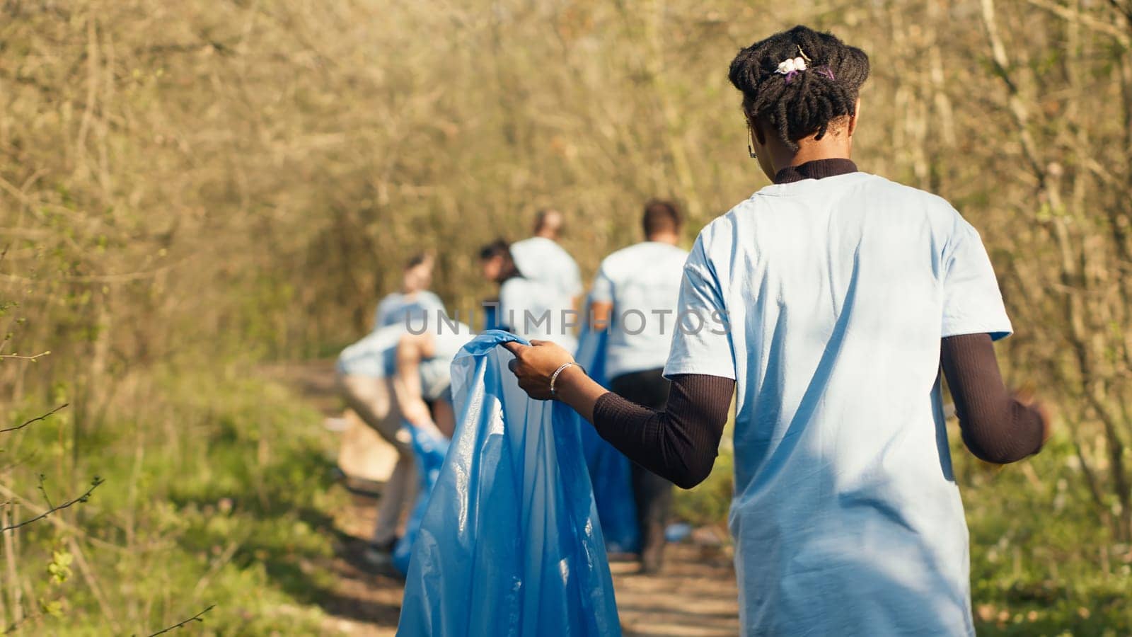African american girl collecting rubbish in a trash bag using tongs by DCStudio