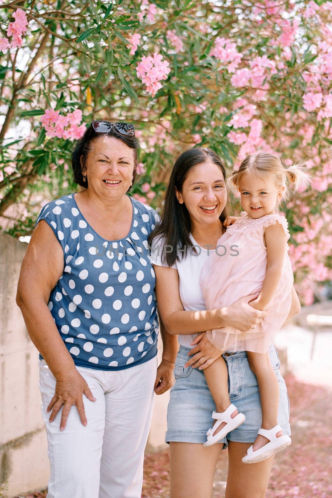 Laughing granny stands next to mom with a little girl in her arms in the garden. High quality photo