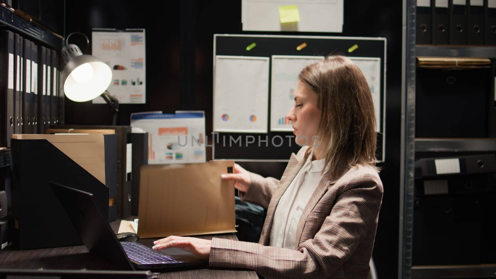Close-up of caucasian female detective closing laptop and folder, leaving her workstation. After obtaining information to solve criminal investigation, policewoman stands and exits the evidence room.