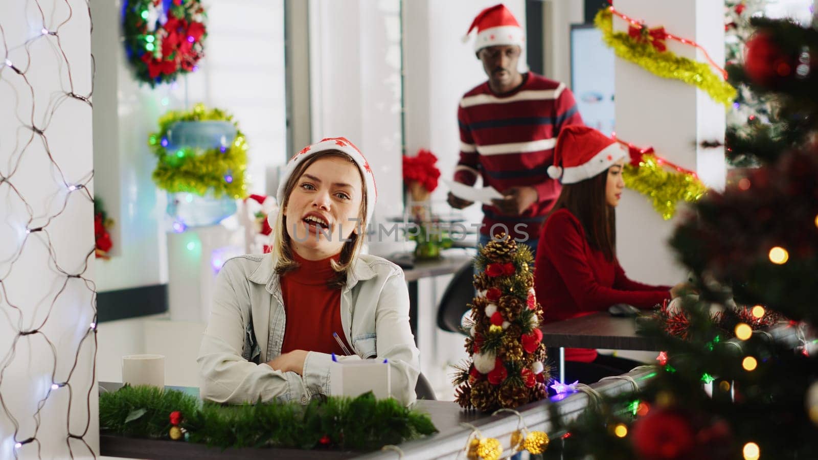 Portrait of cheerful woman in Christmas decorated office participating in company vlog for marketing social media channel, greeting viewers and laughing, enjoying xmas festive mood