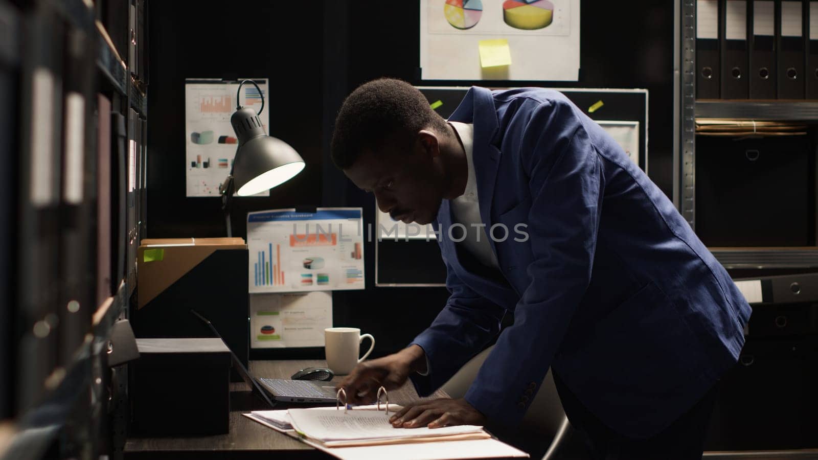 Private investigator grabbing files, analyzing statements, and using laptop to unveil truth in investigation. African american officer utilizing personal computer to cross check with evidence papers.