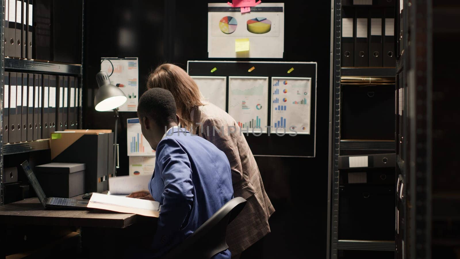 Multiethnic investigators examine evidence, discuss the case, and gather clues in a well-organized environment. Caucasian woman carrying forensic files joins african american man in incident room.