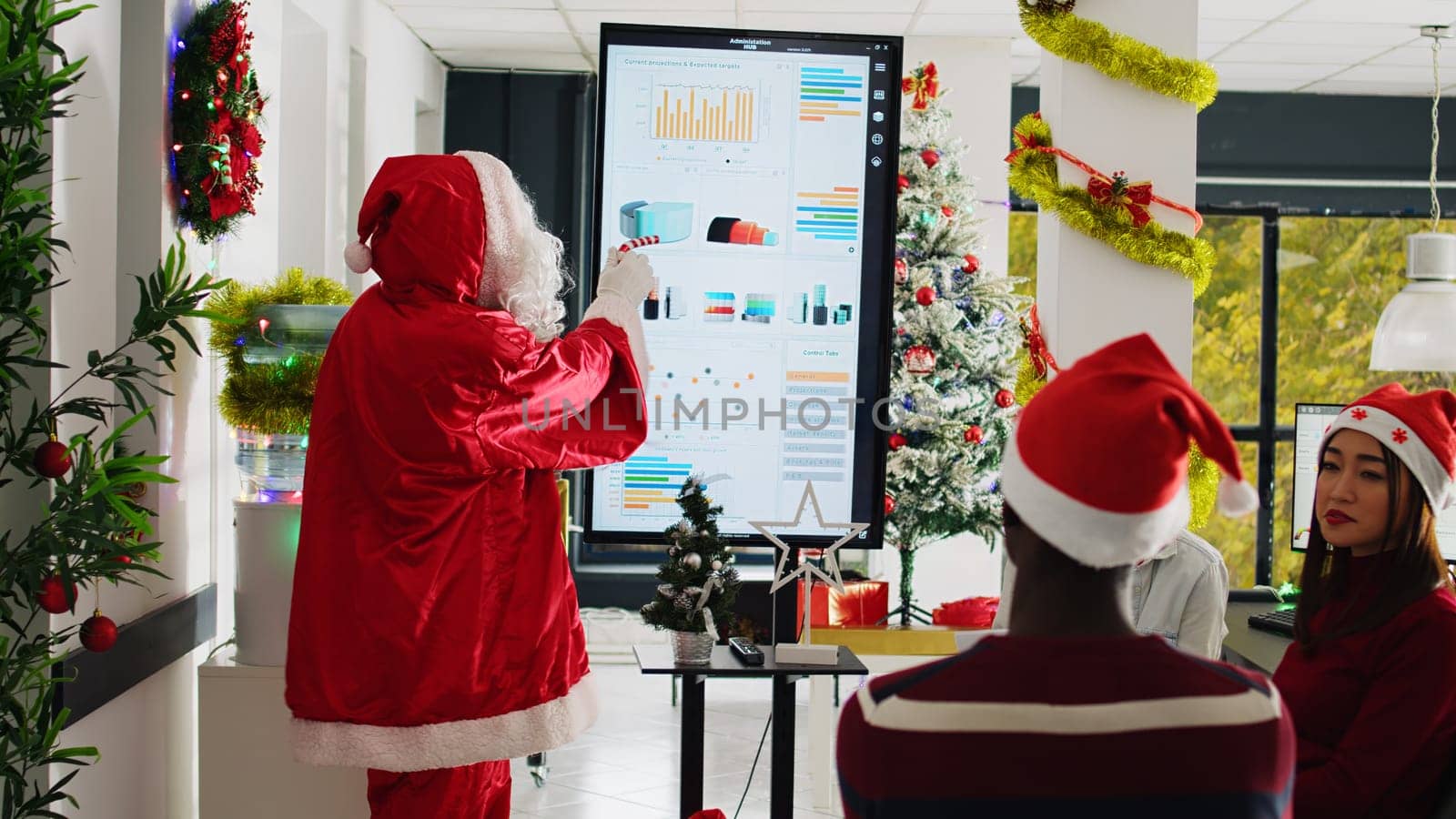 Public speaker dressed as Santa Claus doing presentation in front of company employees in Christmas holiday season. Coworkers in xmas adorn meeting room learning how to advance their career