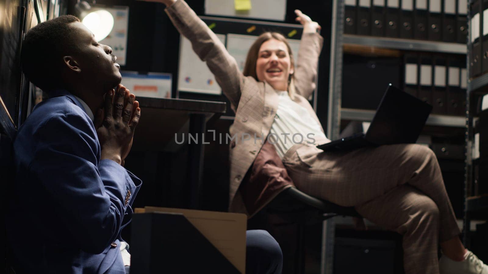 Diverse team of exhausted private investigators in incident room analyze evidence, review files, and conduct research to solve case. Two detectives feeling tired about criminal investigation reports.