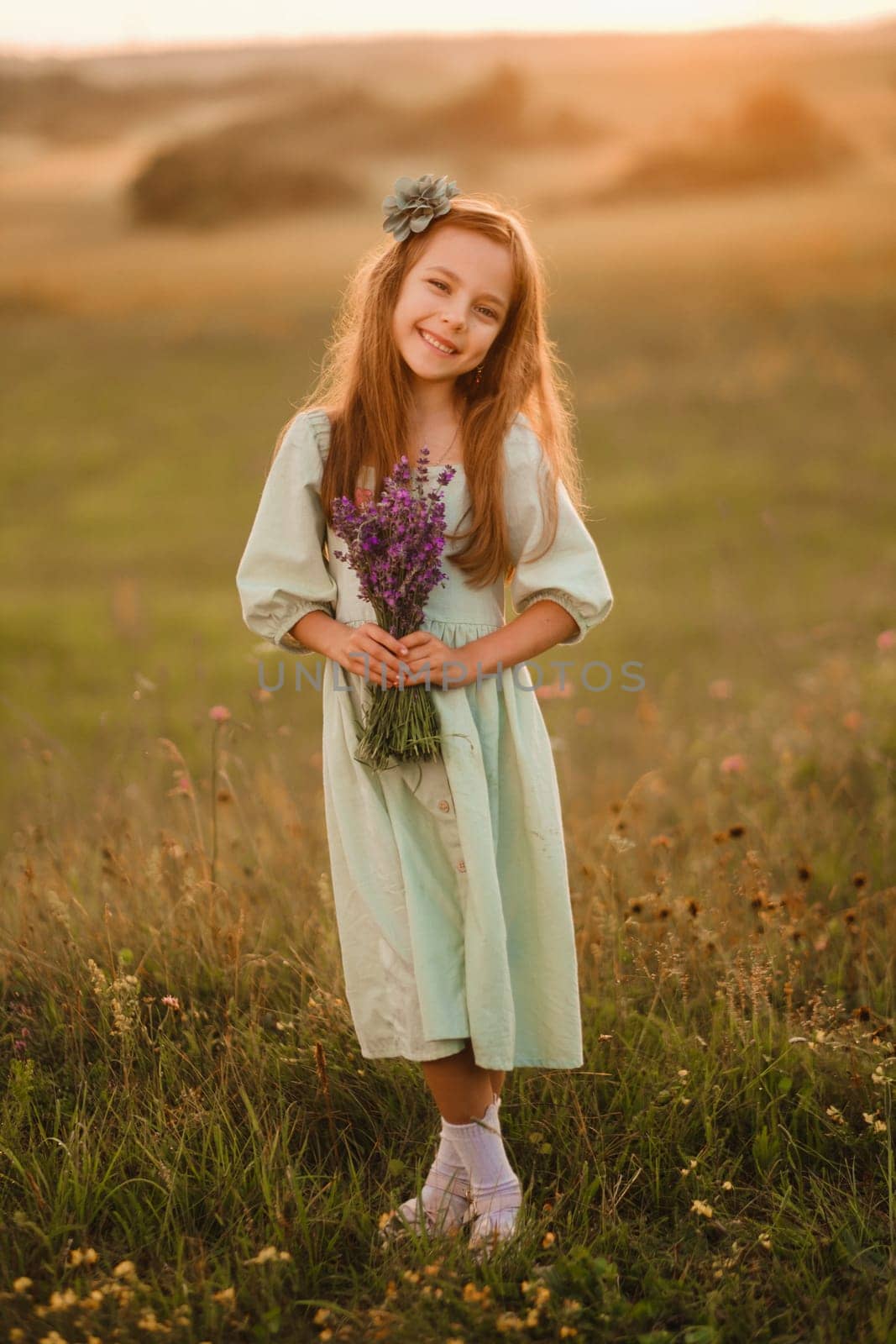 a little girl in a light green dress with a bouquet of lavender in a field at sunset by Lobachad