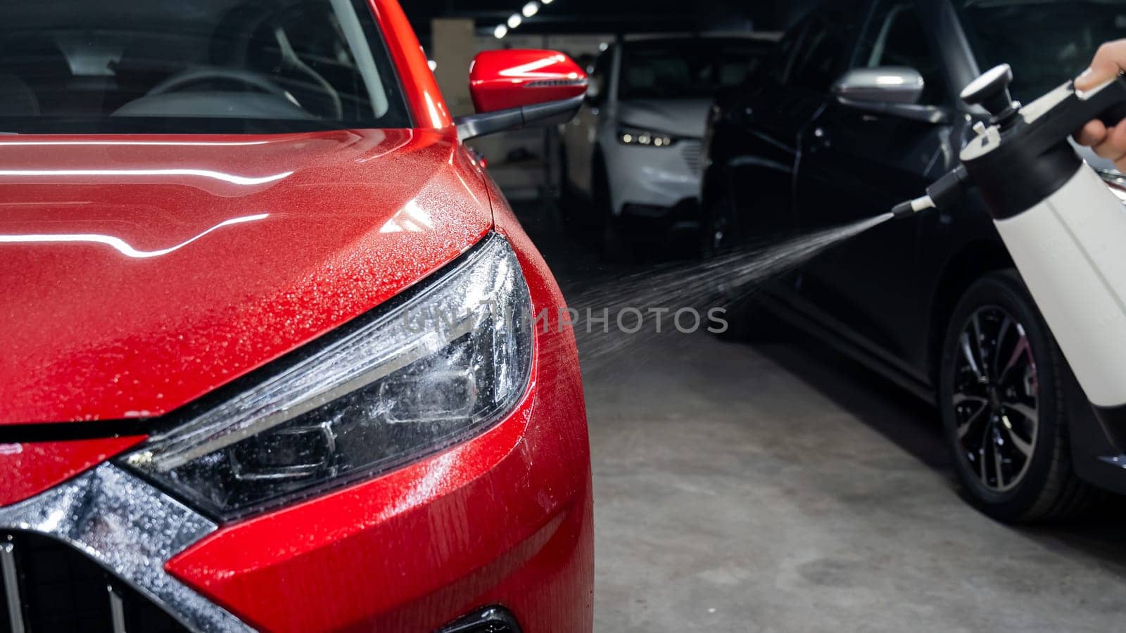 A man washes the headlights of a red car with a spray