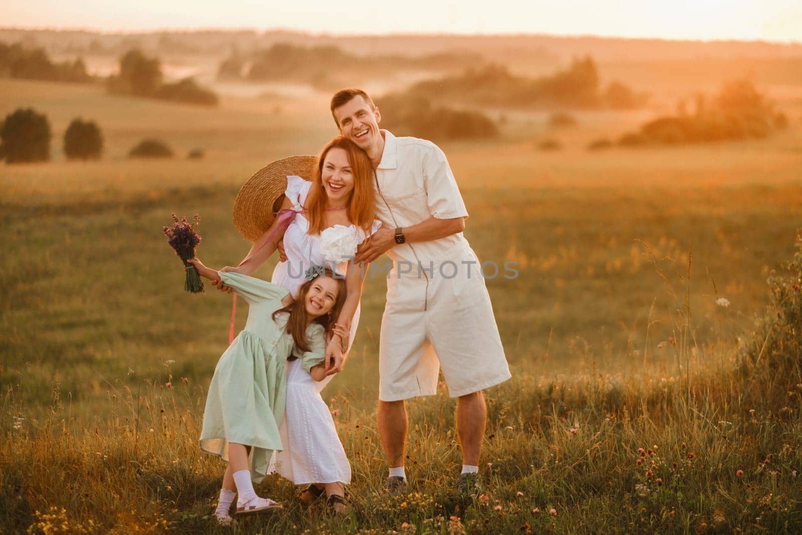 A beautiful happy family of three is standing in a field at sunset.