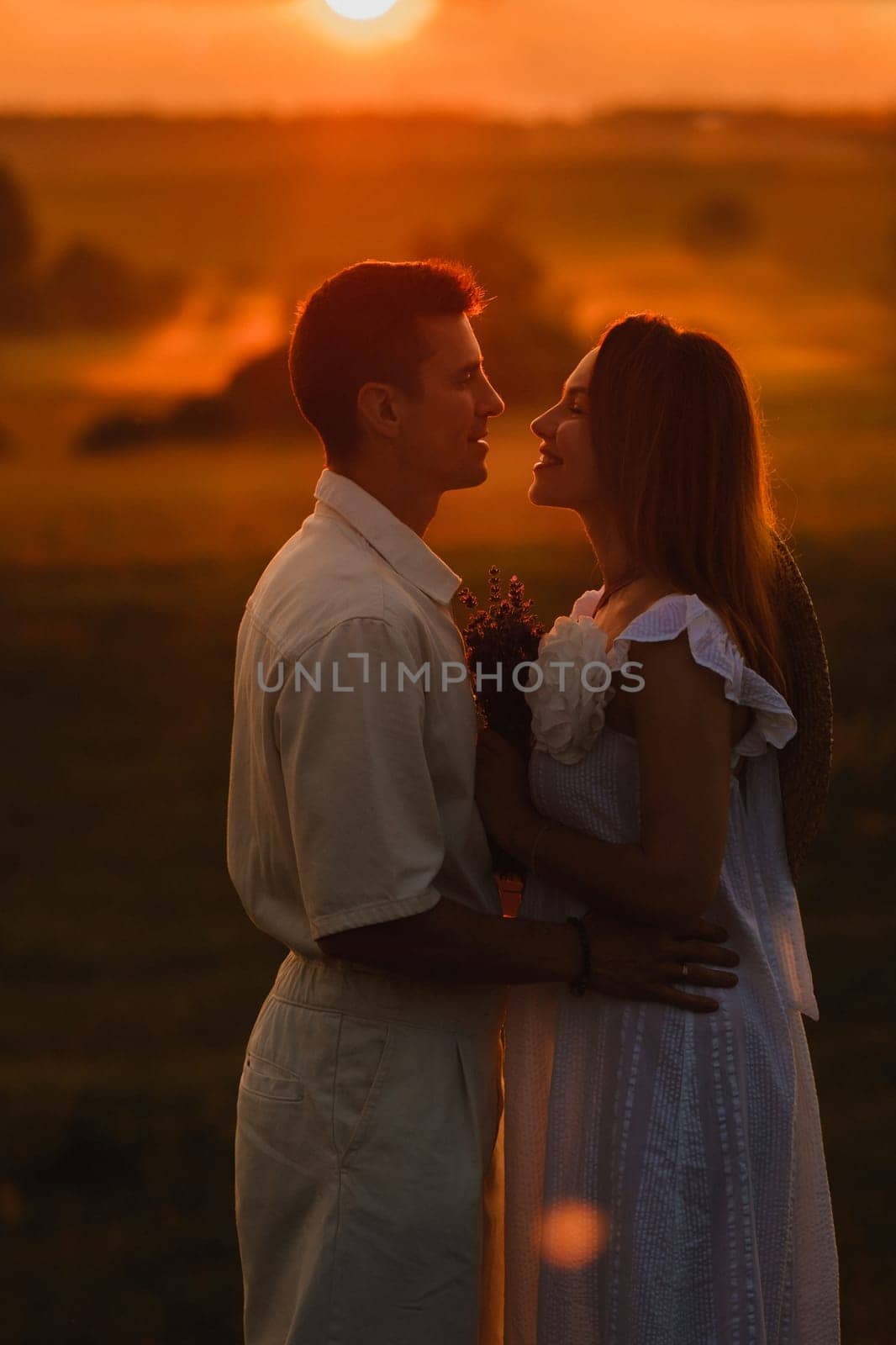 A couple in love in white clothes in a field at a red sunset.