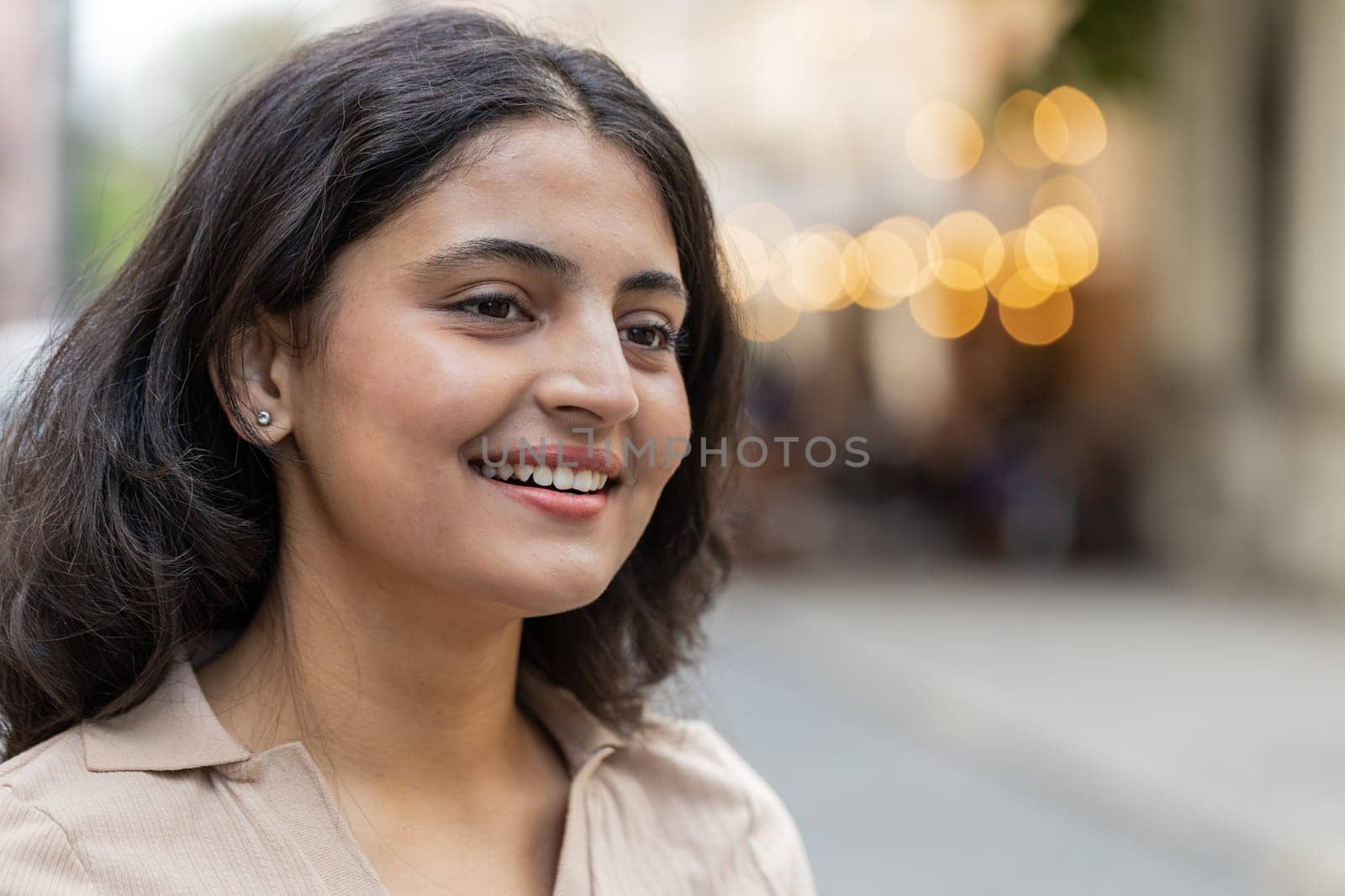 Close-up portrait of happy young Indian woman face smiling friendly open eyes glad expression looking away dreaming resting relaxation feel satisfied good news outdoors. Pretty girl on city street