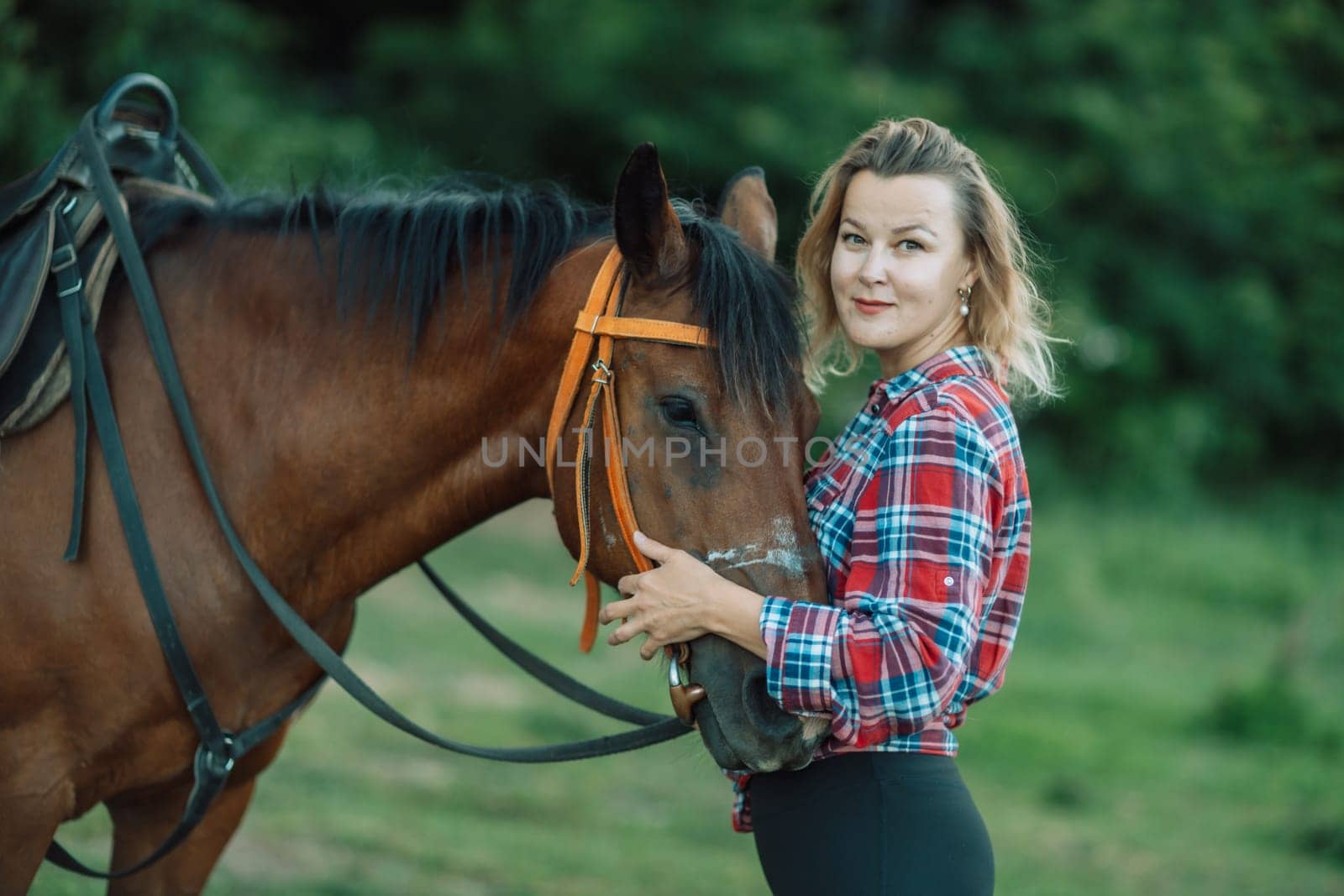 Happy blonde with horse in forest. Woman and a horse walking through the field during the day. Dressed in a plaid shirt and black leggings. by Matiunina