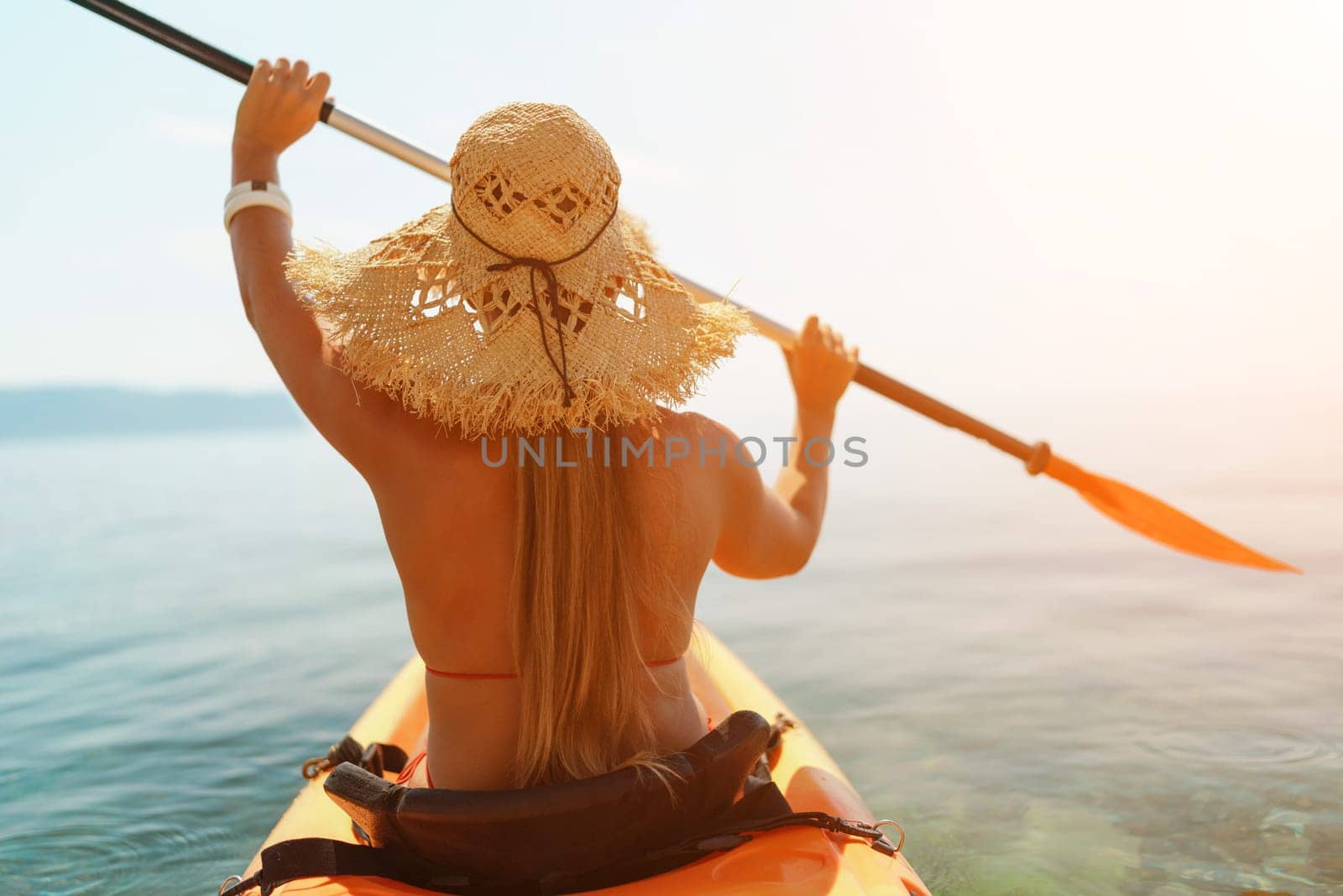 A woman wearing a straw hat is paddling a canoe on a sunny day. Scene is relaxed and carefree, as the woman enjoys her time on the water