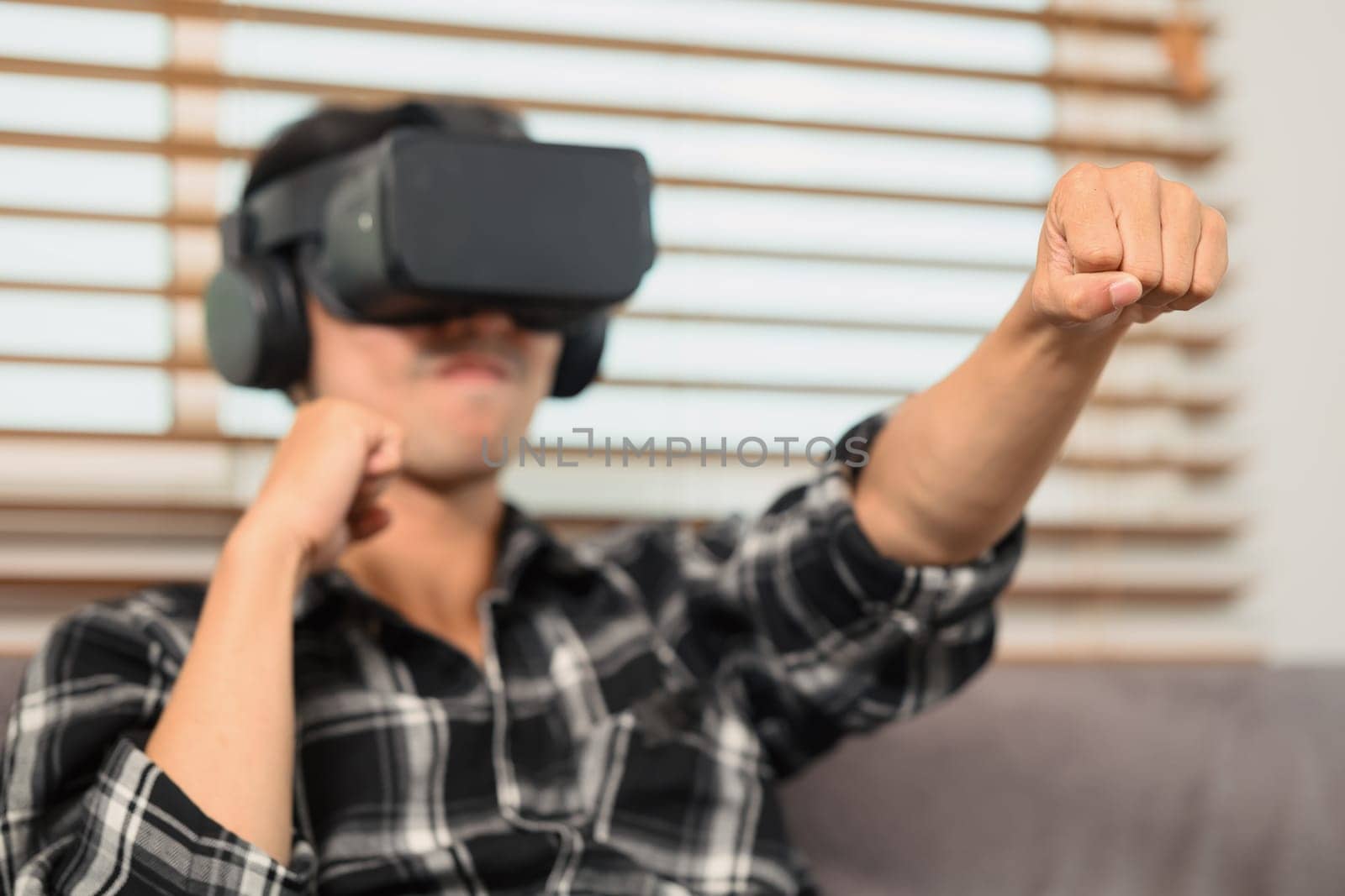 Excited man with VR headset playing boxing game and throwing punches in the air by prathanchorruangsak