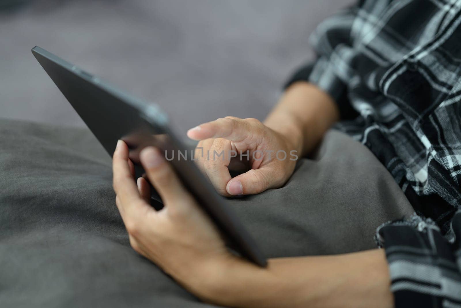Closeup hand of young man using digital tablet while sitting on couch at home.