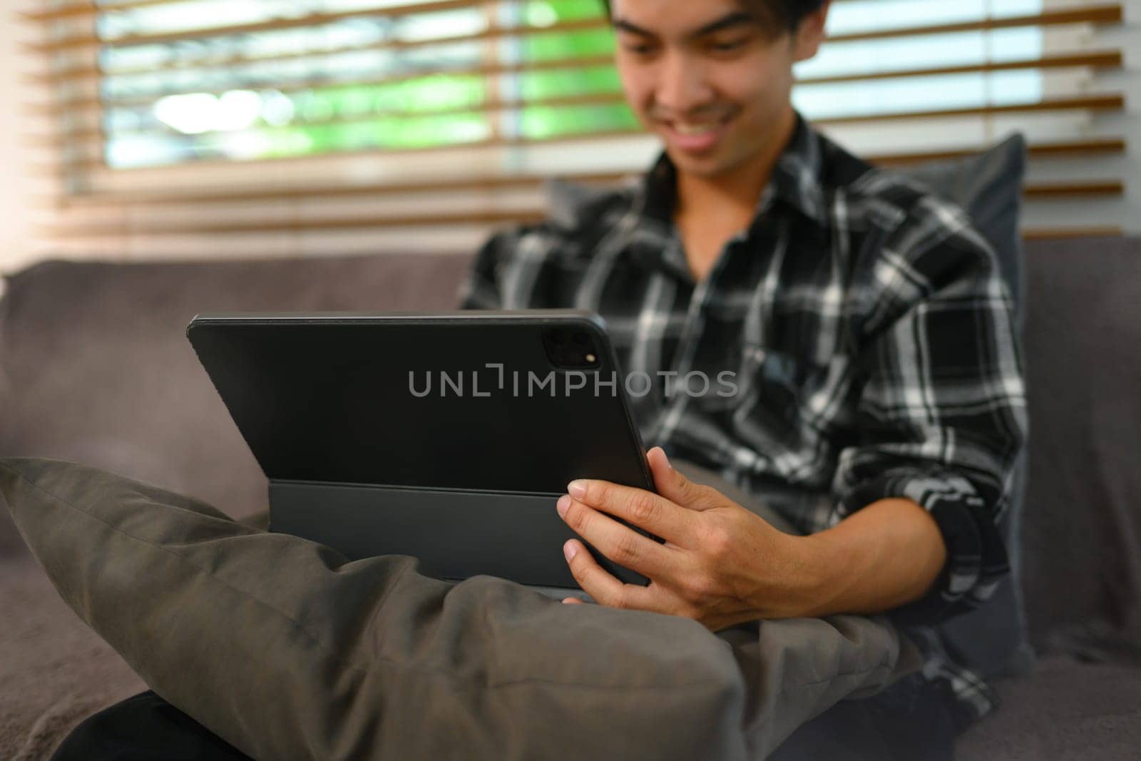 Selective focus. Hand of young man using digital tablet while sitting on couch at home by prathanchorruangsak