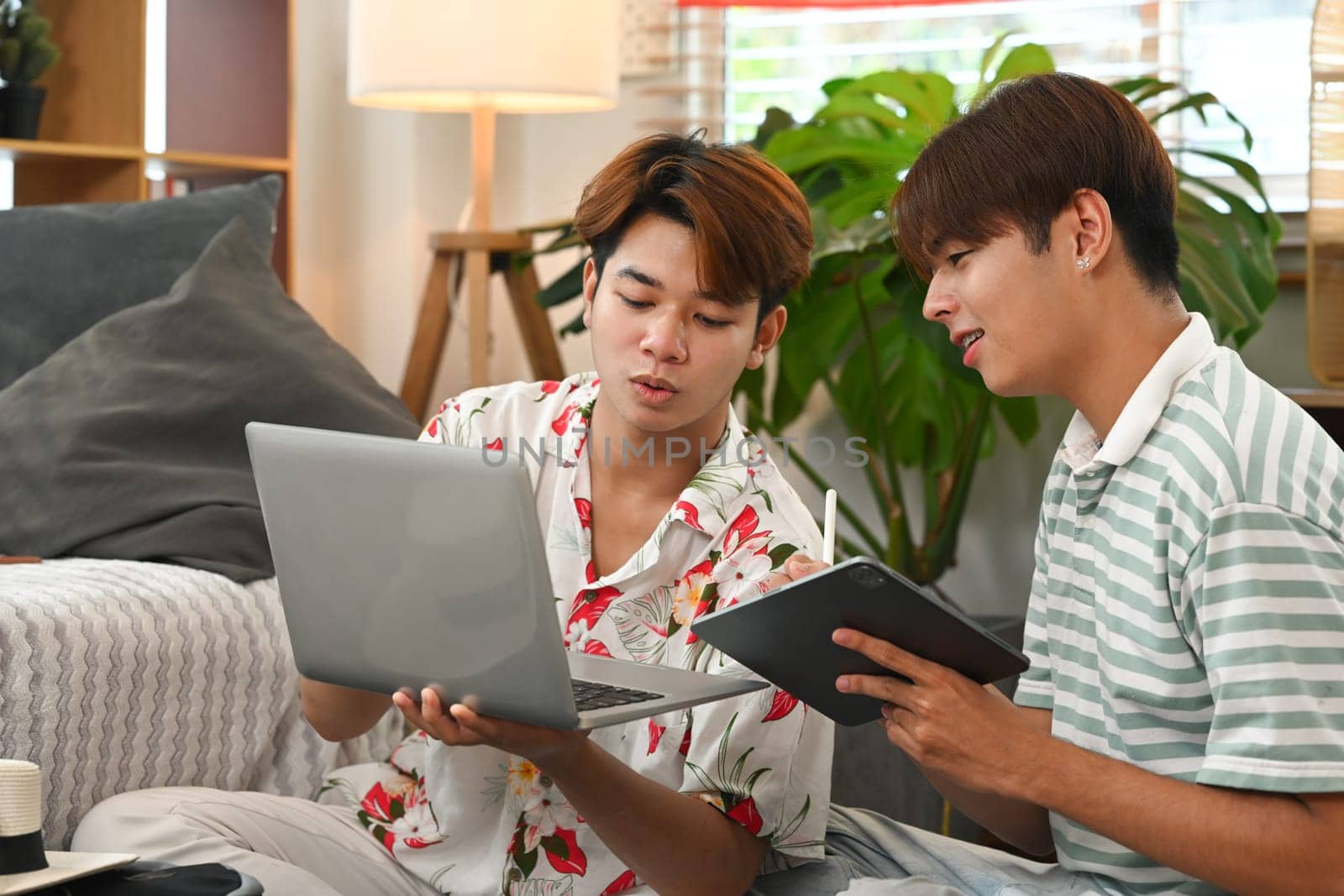 Happy young gay male couple planning vacation trip, using laptop for booking a hotel on website.