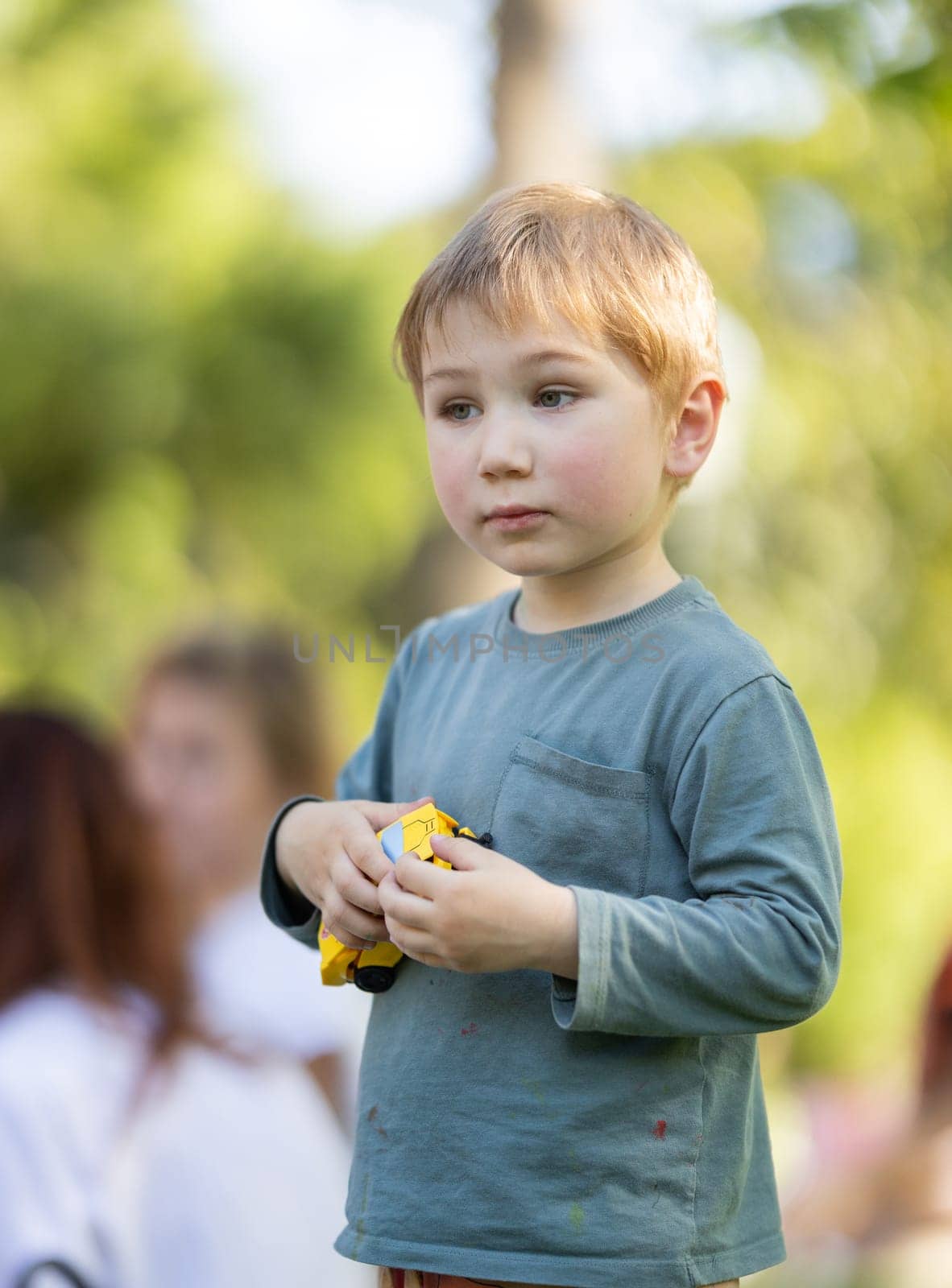 A young boy is holding a toy car in his hand. He is wearing a green shirt and has a serious expression on his face
