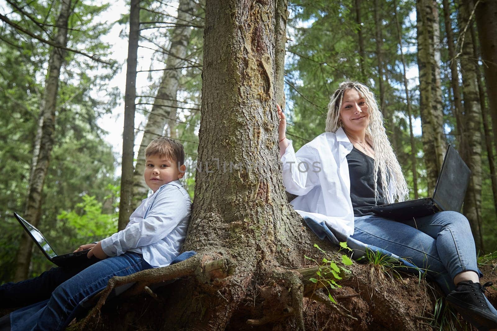 Mother and son with a laptops in forest in summer. Fat young smart teenage boy and woman working with modern IT technologies in nature by keleny