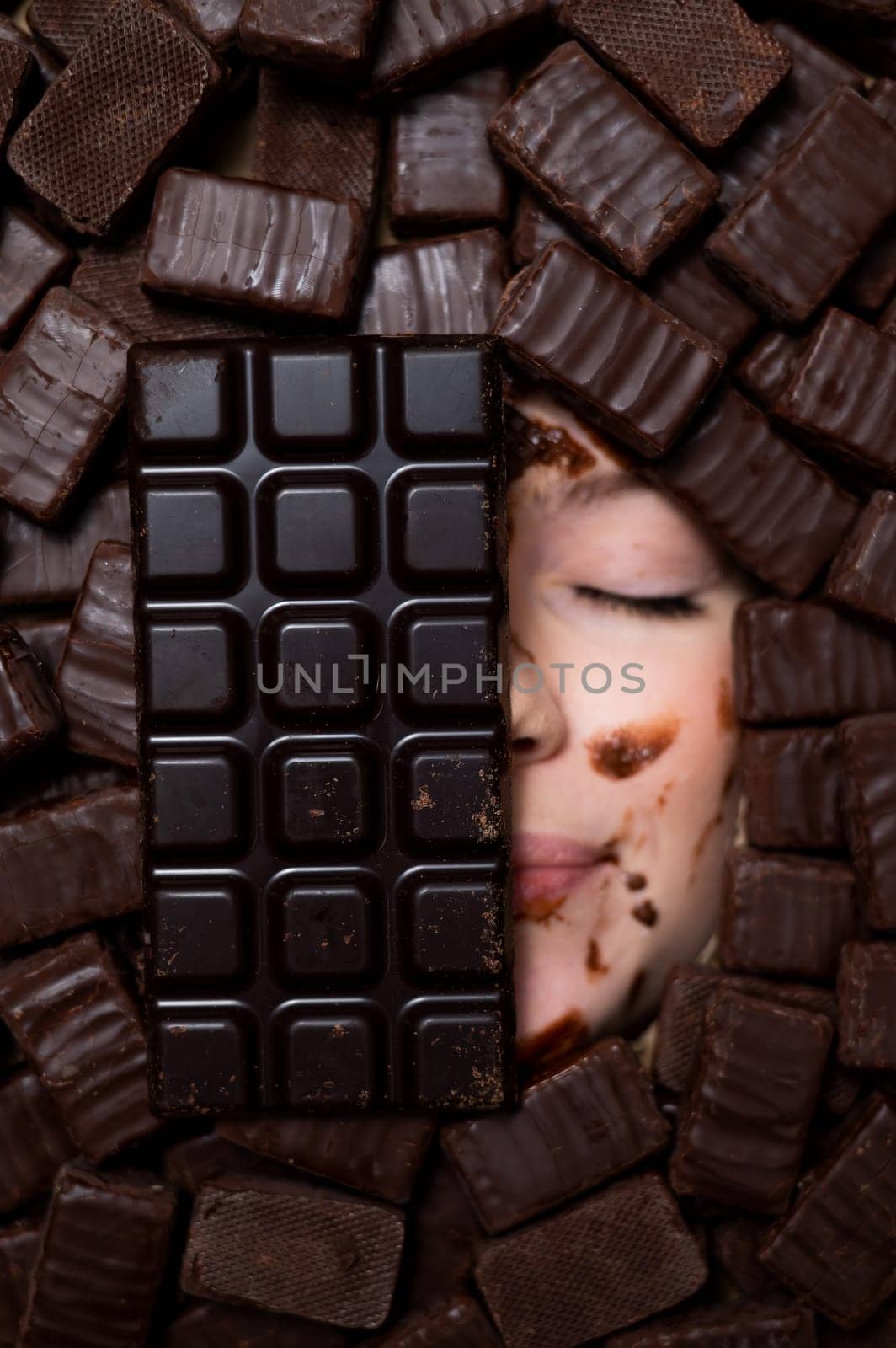 The face of a caucasian woman surrounded by sweets. The girl is smeared in chocolate