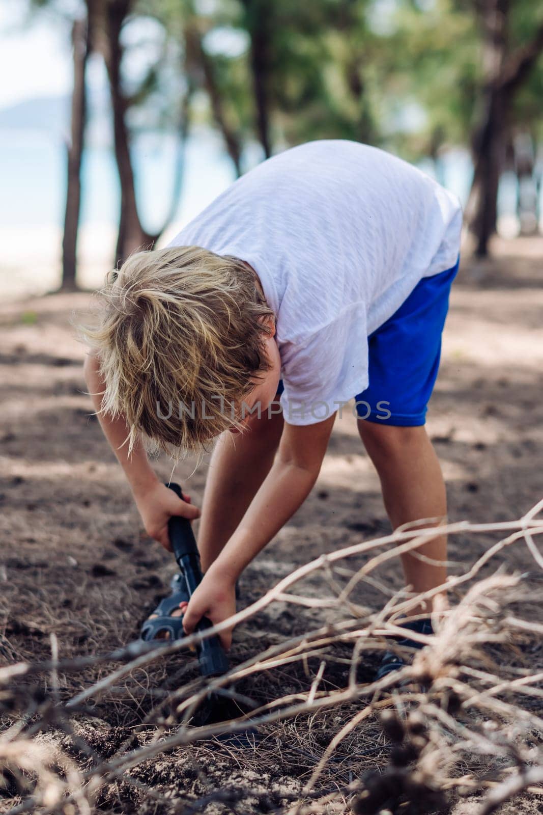 Cute boy digging soil in forest near sea beach. Family natural education skills. Travelling together. Learning camping organizing bonfire.