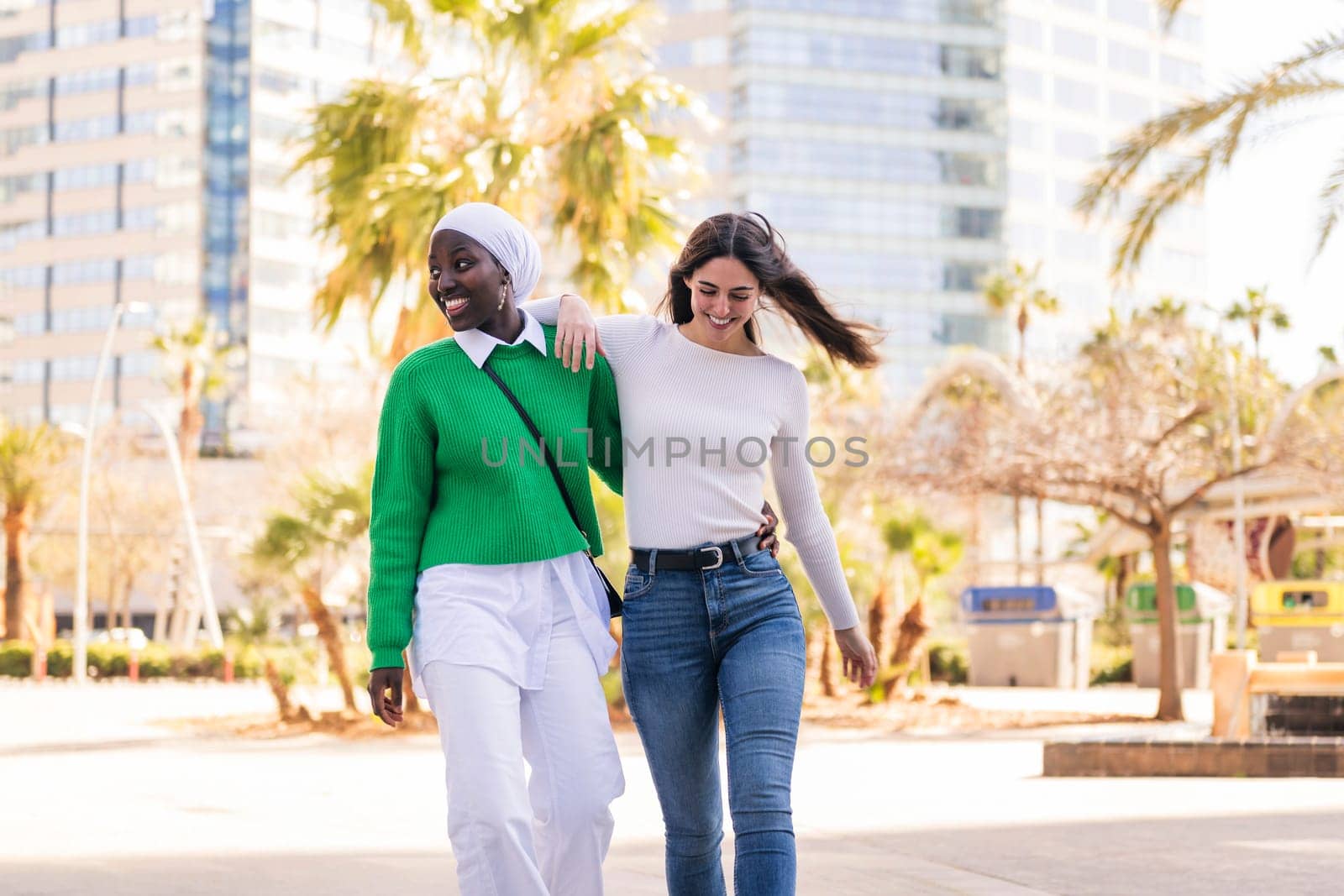 young multiracial couple of two women walking smiling happy through the city hugging, concept of diversity and modern lifestyle, copy space for text