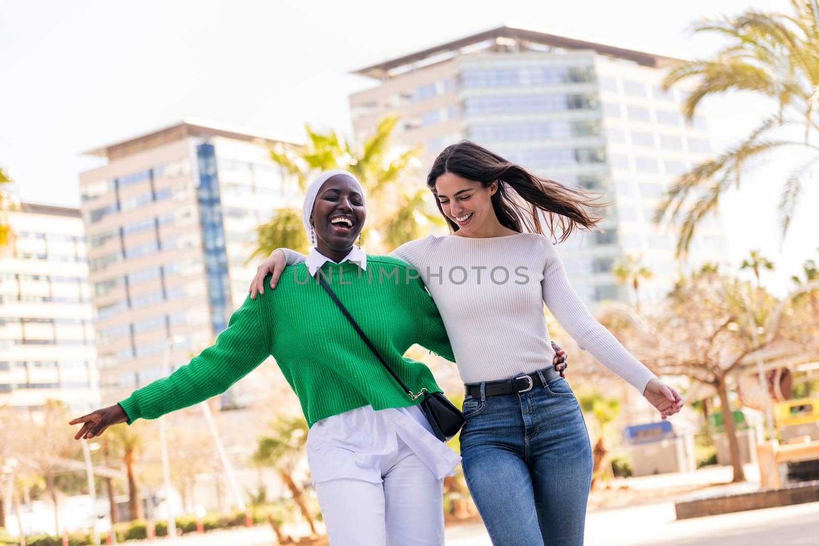 young multiracial couple of two women walking laughing happy and having fun through the city while hugging, concept of diversity and modern lifestyle, copy space for text