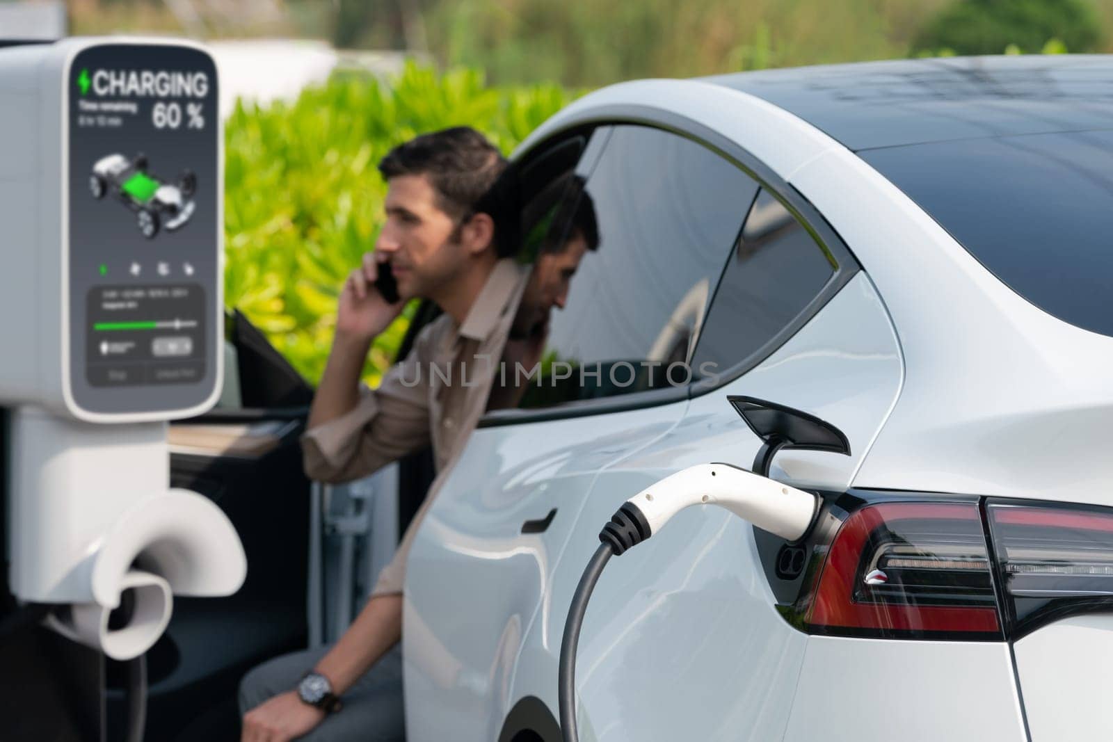 Young man recharge EV electric vehicle at green city park. Expedient by biancoblue