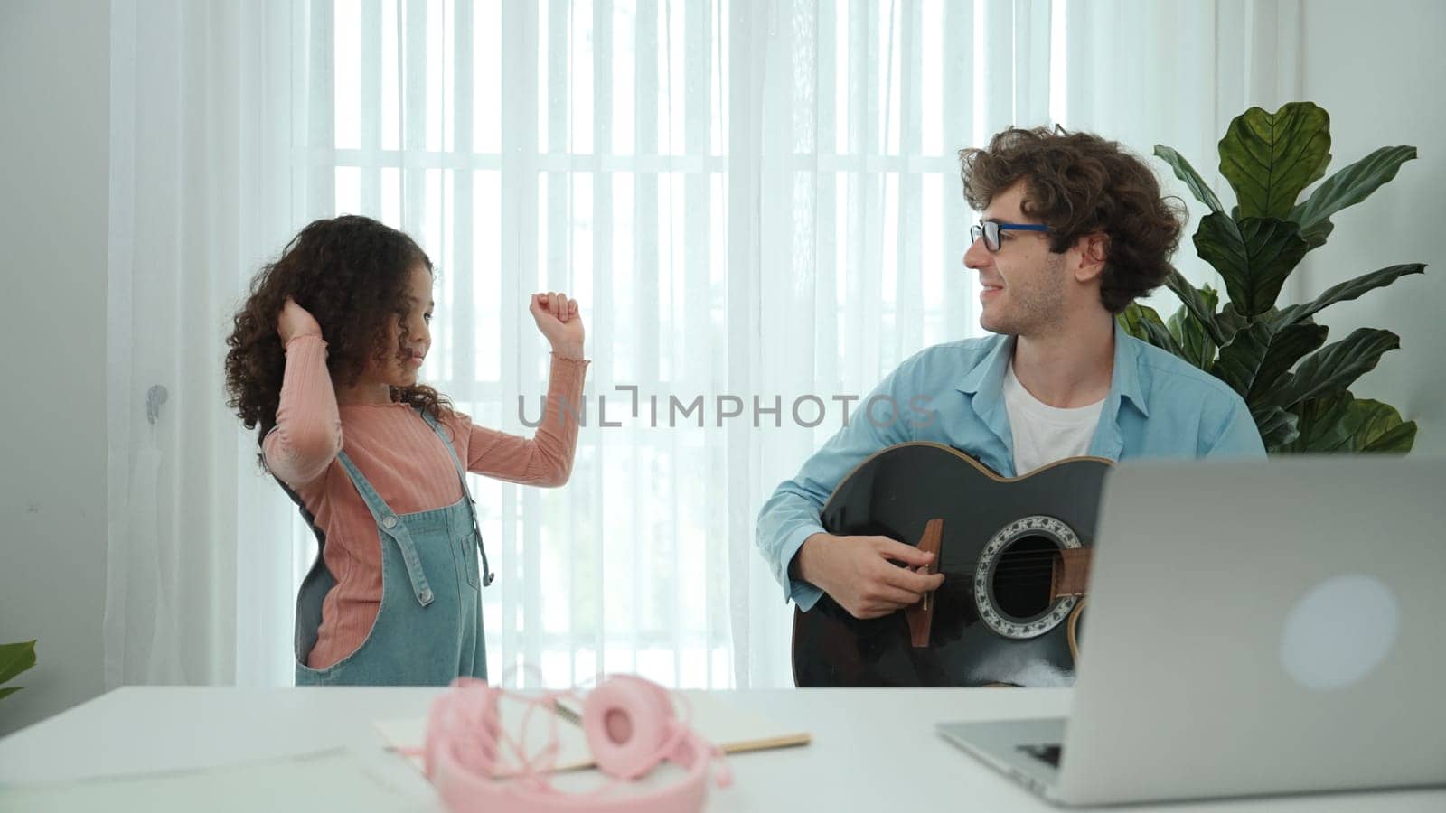 Happy schoolgirl with headphone standing and dancing to acoustic music while dad playing guitar. Smiling child move to music while enjoy to listening father song. Family recreation concept. Pedagogy.