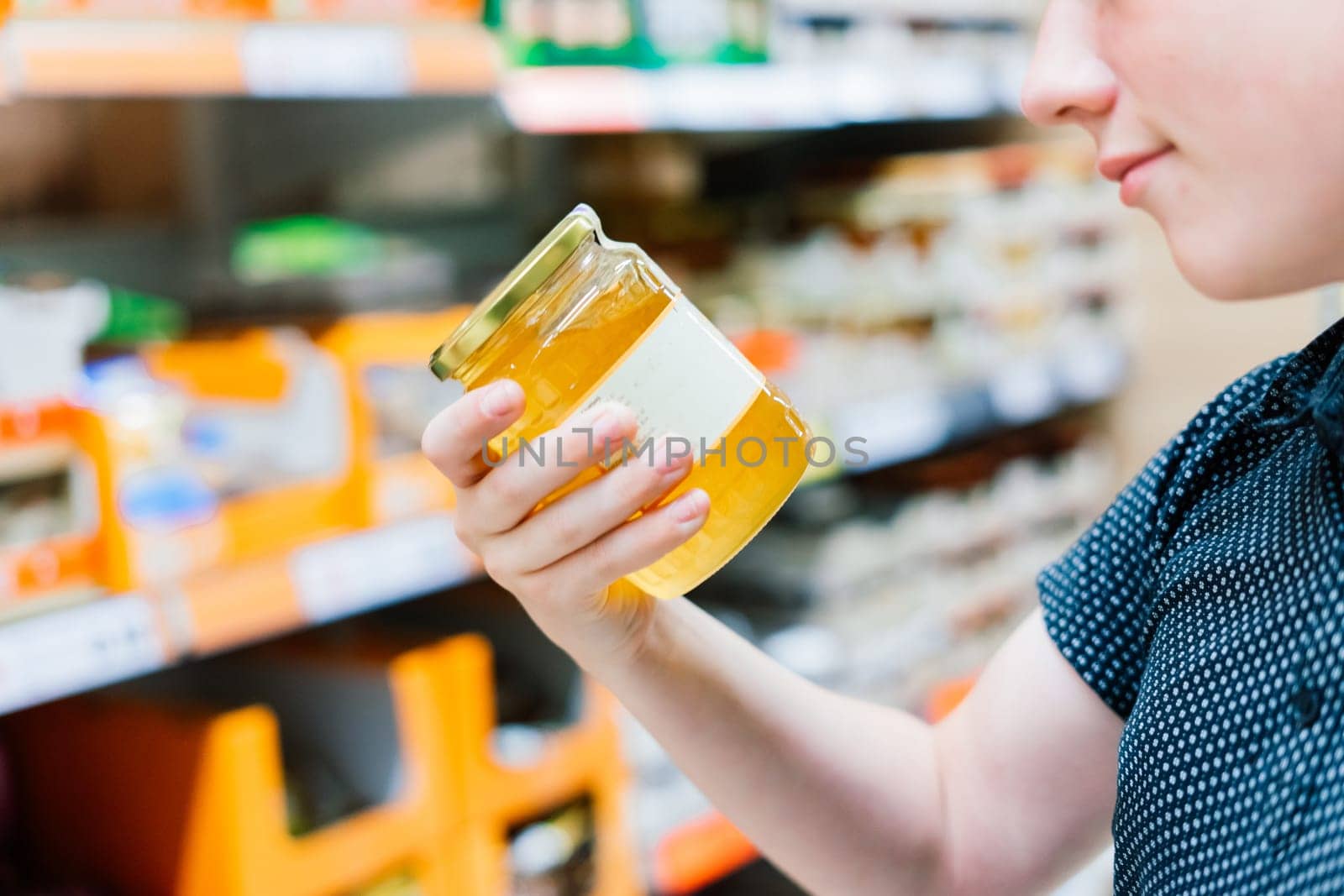 Young male hand holds honey on a blurred background, a row of shelves with groceries in supermarket by Zelenin