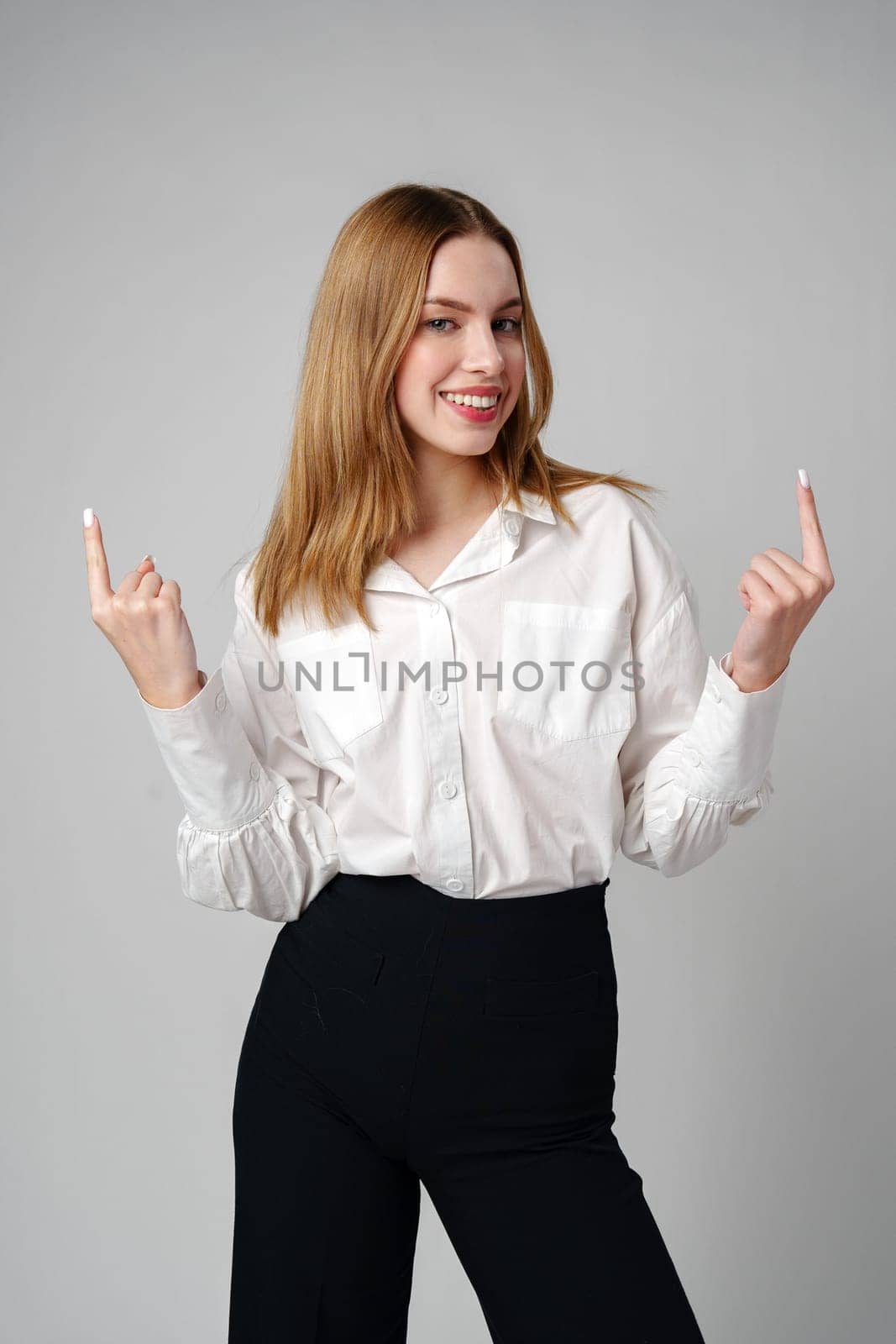 Young businesswoman standing against gray background and pointing her finger to copy space. High quality photo