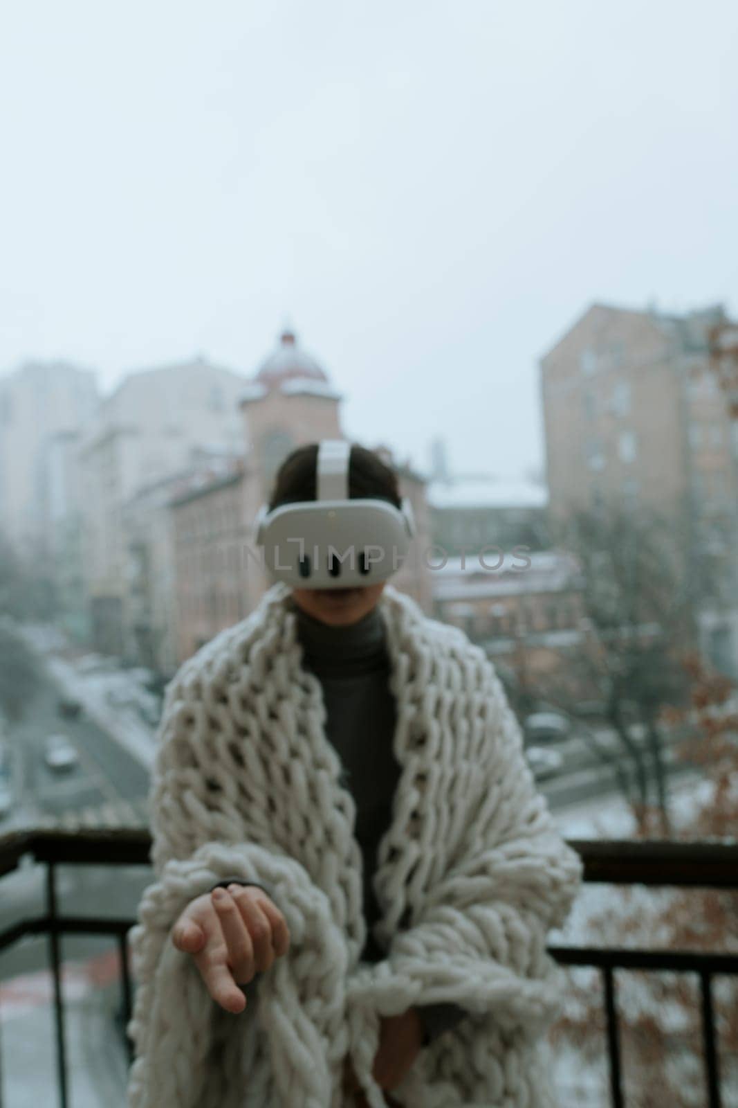 A young woman in a virtual reality headset stands on the balcony in winter. by teksomolika