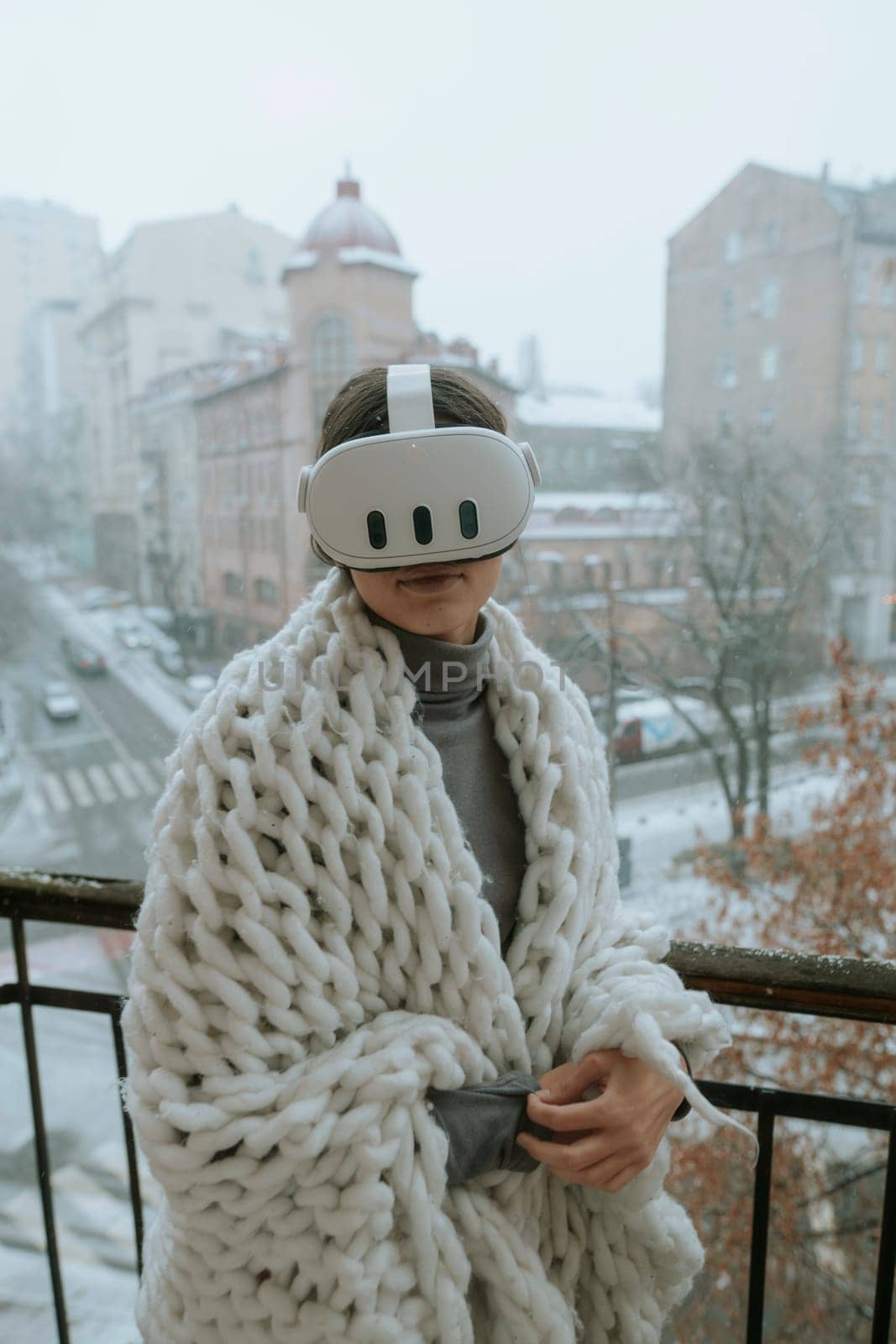 A girl immerses herself in virtual reality on the winter balcony, wearing a headset. High quality photo