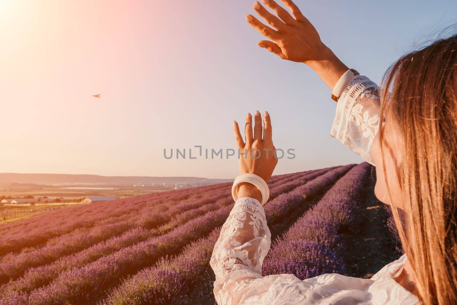 Close up portrait of young beautiful woman in a white dress and a hat is walking in the lavender field and smelling lavender bouquet.