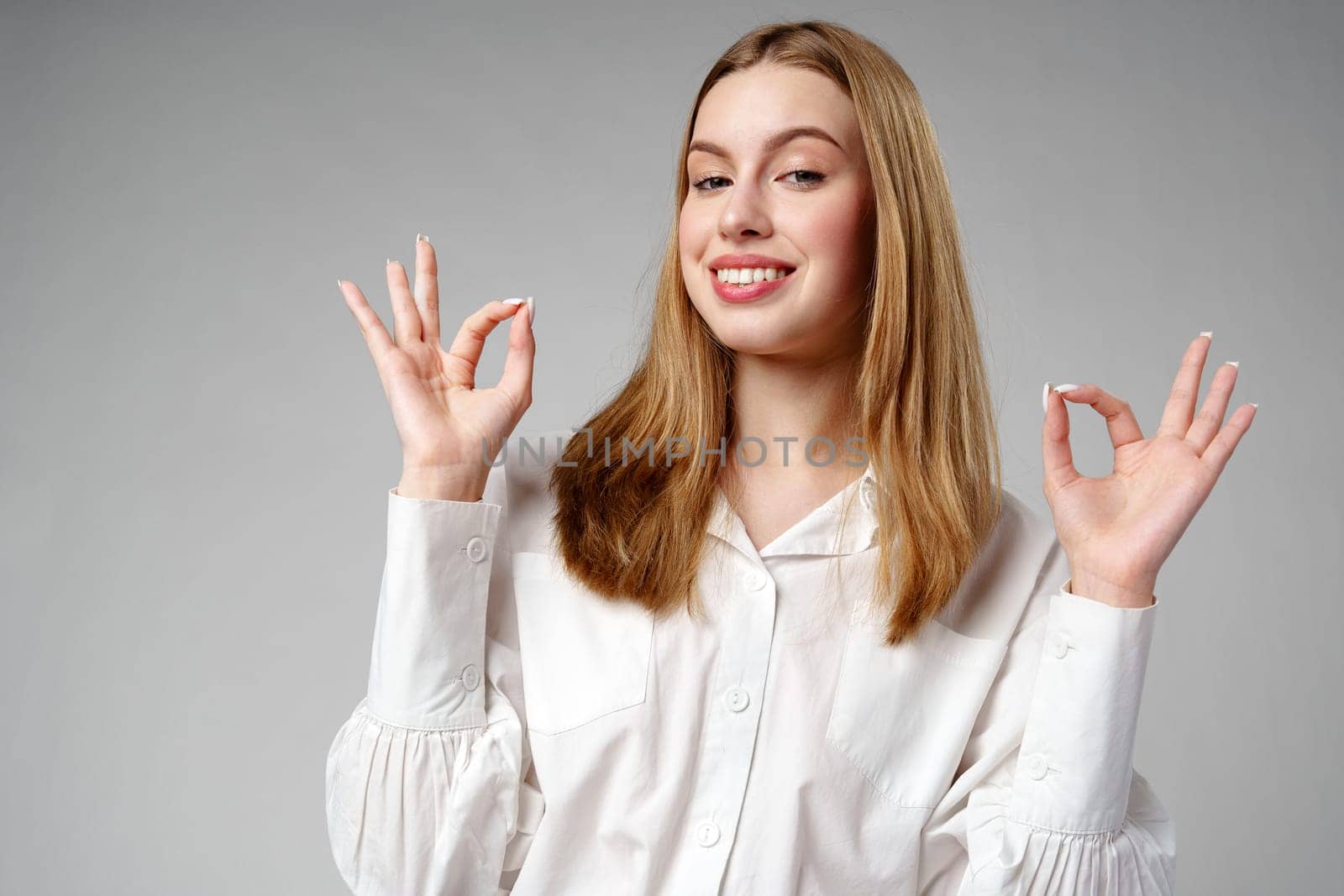 Young Woman Gesturing OK Sign With Hand Against a Neutral Background in studio