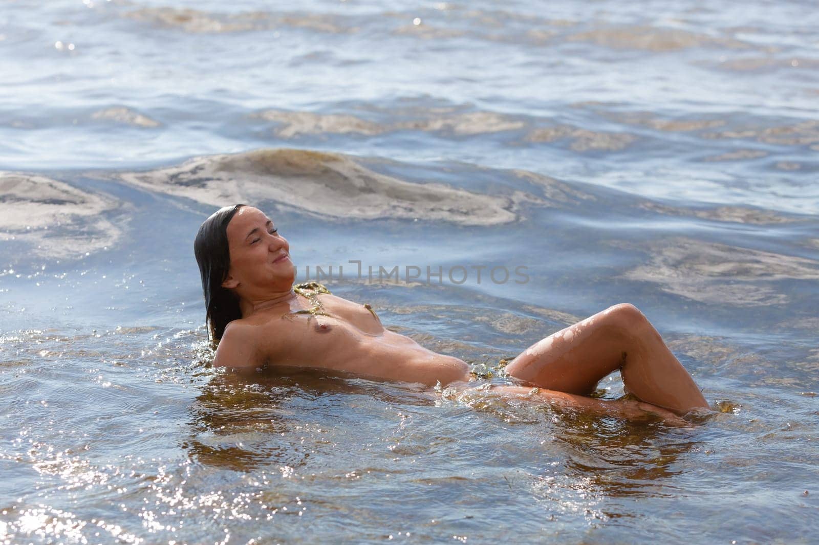 Young beautiful woman posing nude on the seaside enjoying the sea and nature