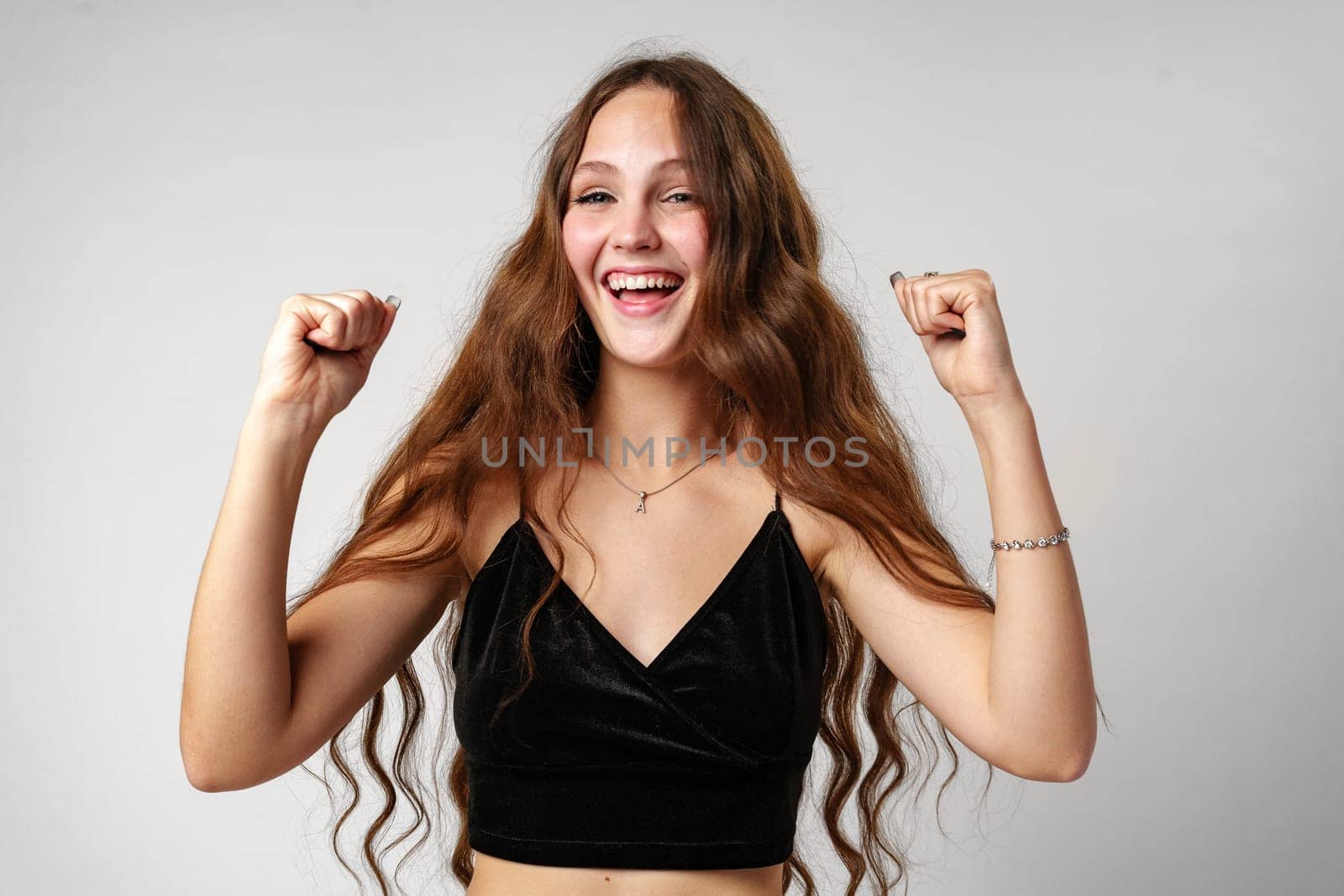 Young Woman Celebrating Victory With Raised Fists on a Plain Background by Fabrikasimf