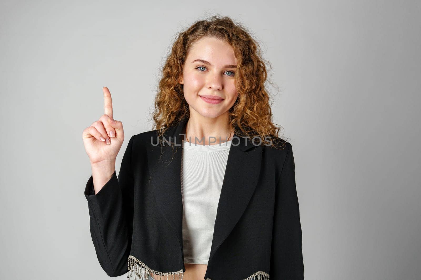 Young Woman in Black Jacket Pointing Up in Studio