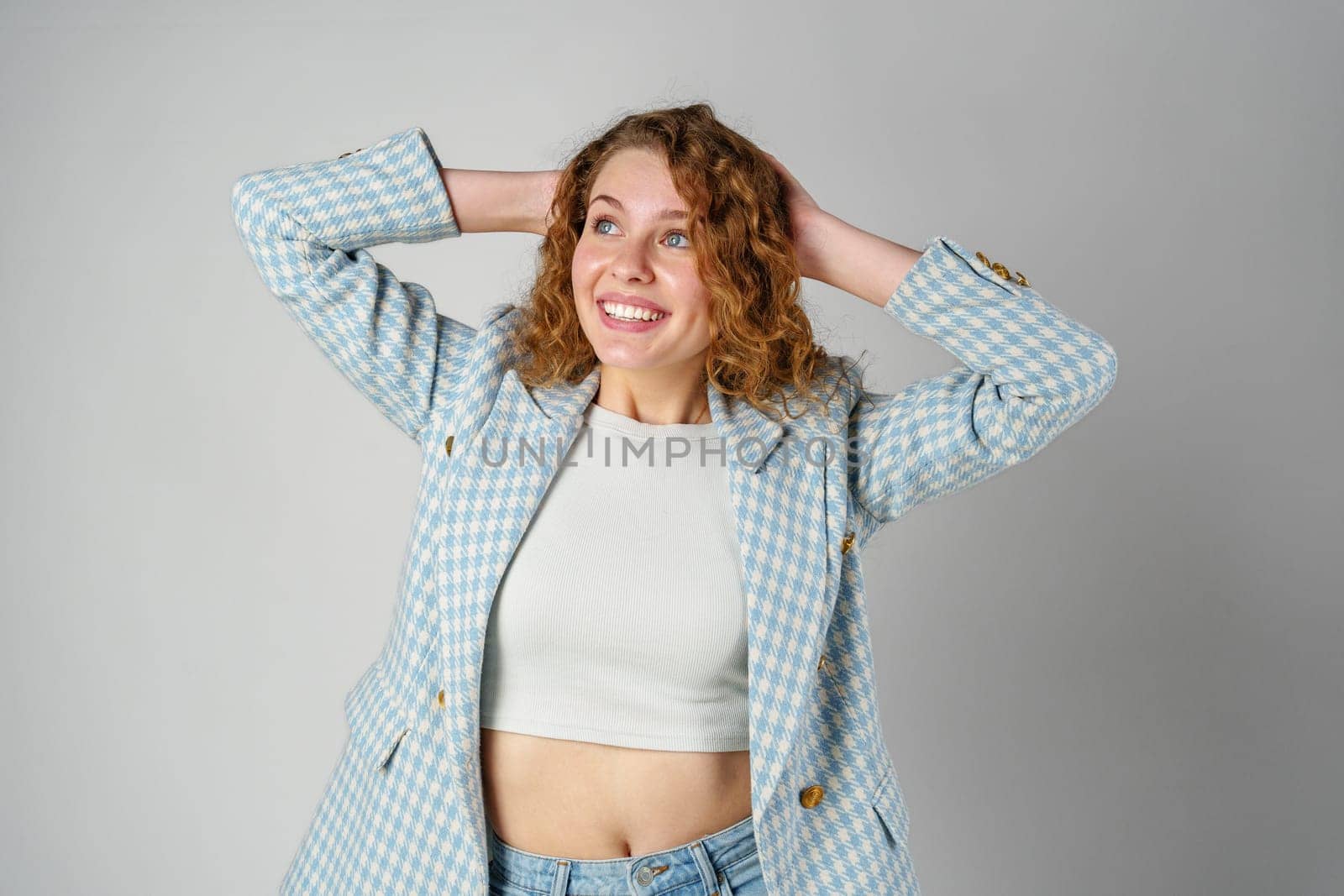 Young woman with curly hair in blue jacket posing on gray background close up
