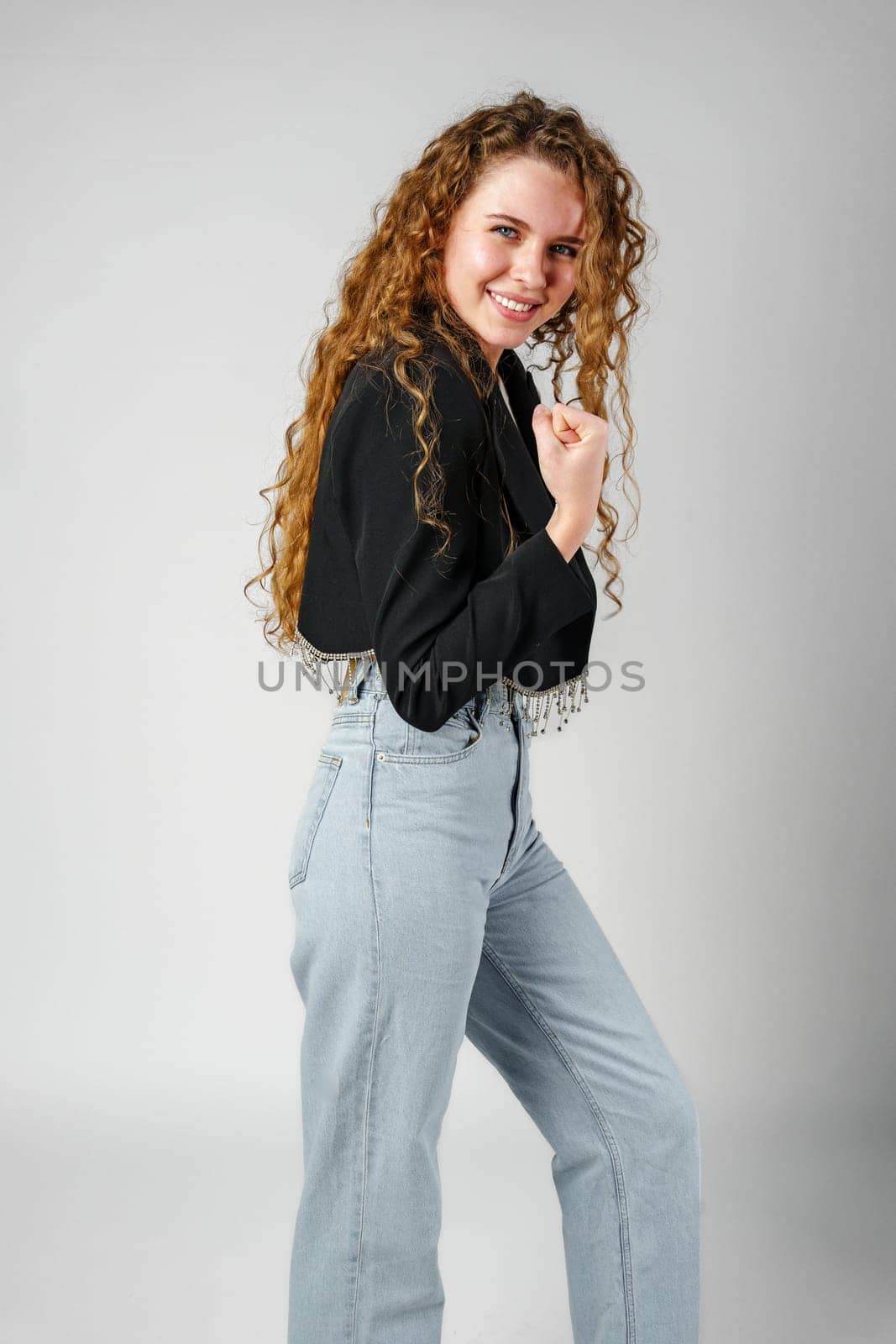 Excited Young Woman Celebrates Success With Raised Fists Against a Gray Background by Fabrikasimf